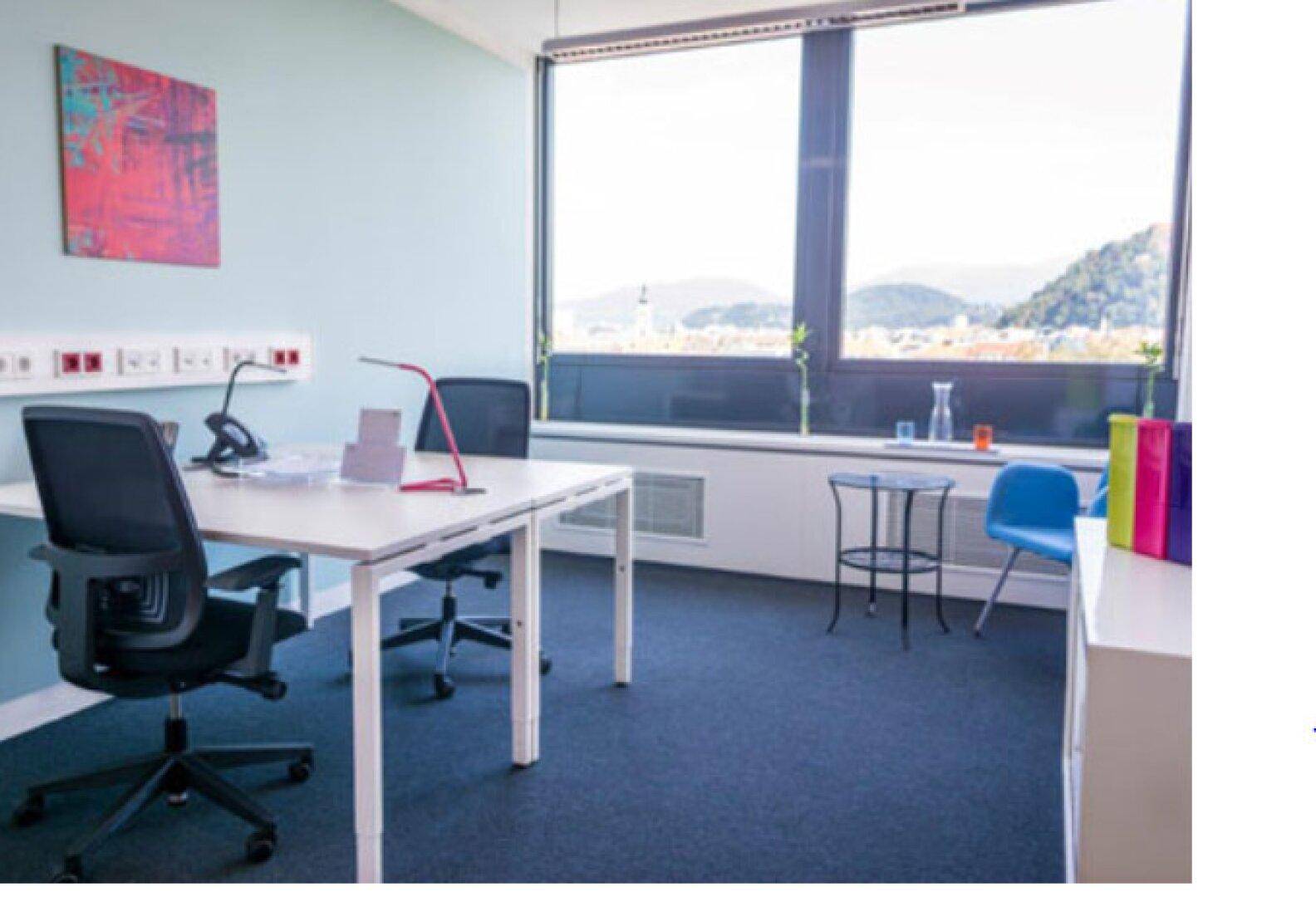 Helles Büro mit Schreibtisch und Stuhl, großen Fenstern und einem beeindruckenden Blick auf die Berge.