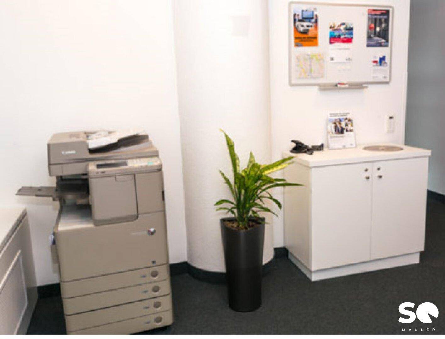 Praktischer Bereich mit Kopierer, Spülbecken und Whiteboard, ideal für Büromaterial und Drucker.