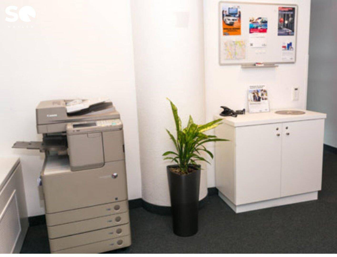 Bürobereich mit großem Kopierer, kleiner Küchenzeile und Whiteboard für Notizen.