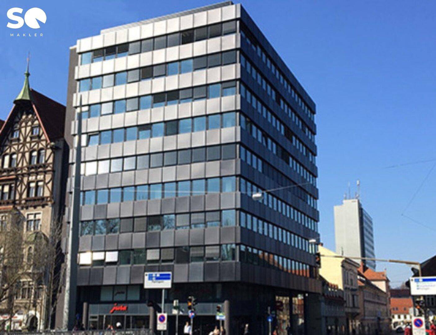 Zeitgenössisches Bürogebäude mit Glasfassade und Metallpaneelen in urbaner Umgebung.