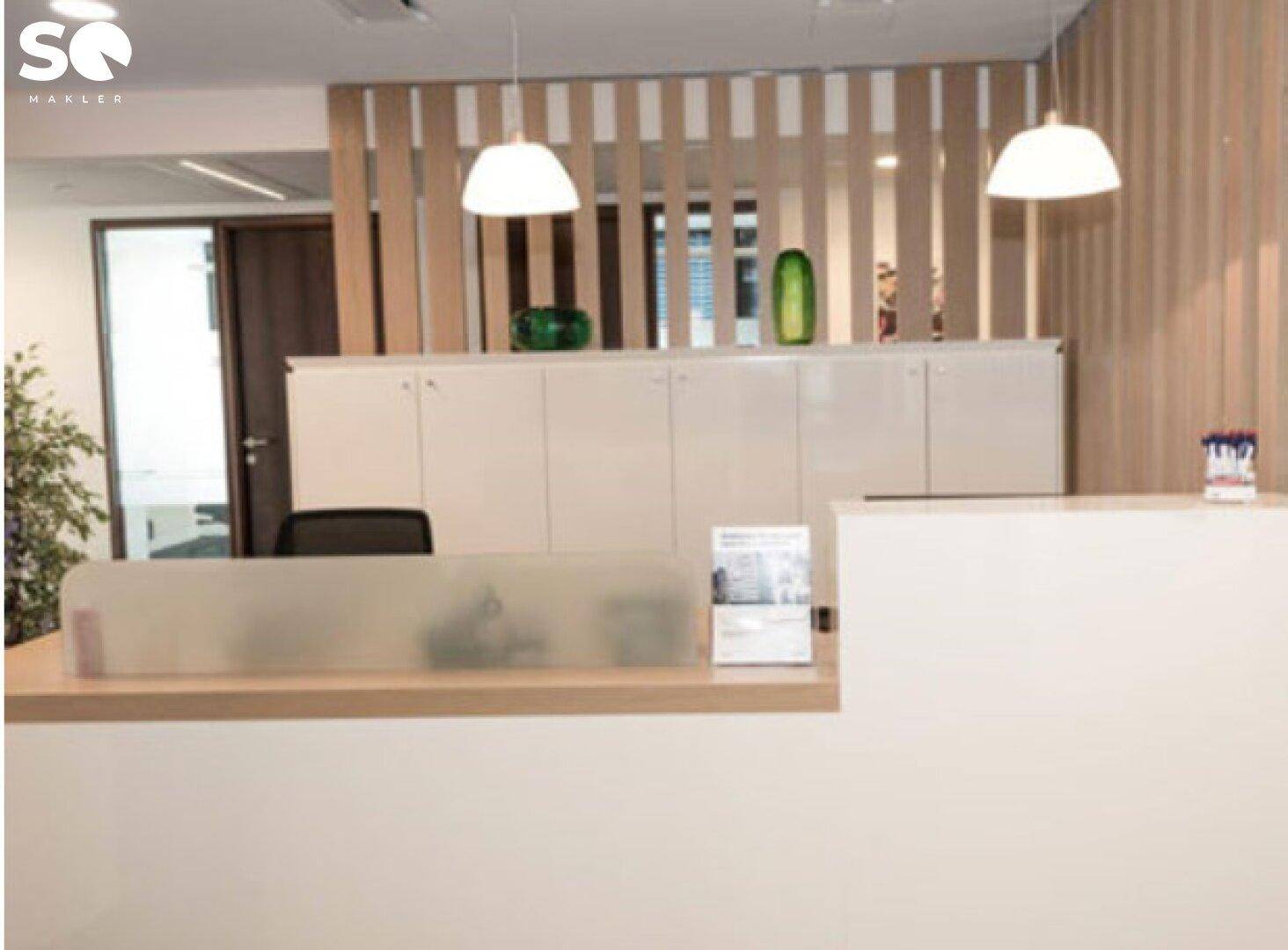Empfangsbereich mit heller Holzlamellenwand, moderner Theke und dekorativen Elementen.