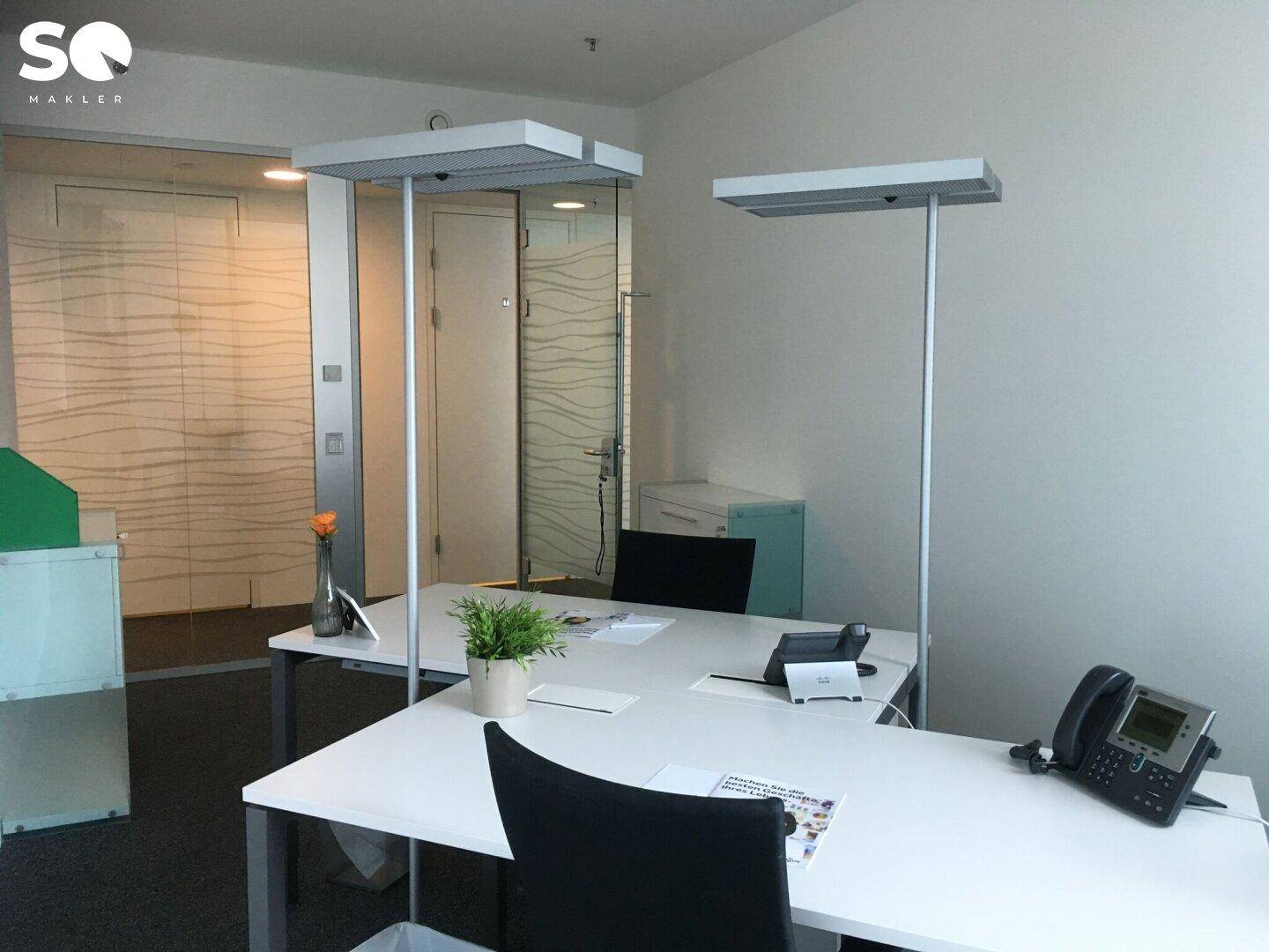 Büroraum mit zwei Arbeitsplätzen, Stehleuchten und eleganten Glasabtrennungen im Hintergrund.