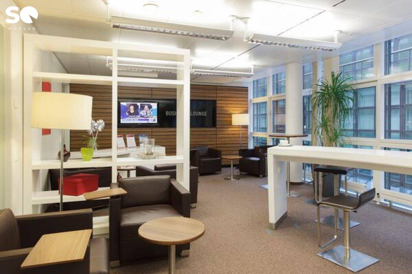 Gemütliche Business-Lounge mit Ledersesseln, hohen Fenstern und einem Bartresen für entspannte Pausen im Bürogebäude.