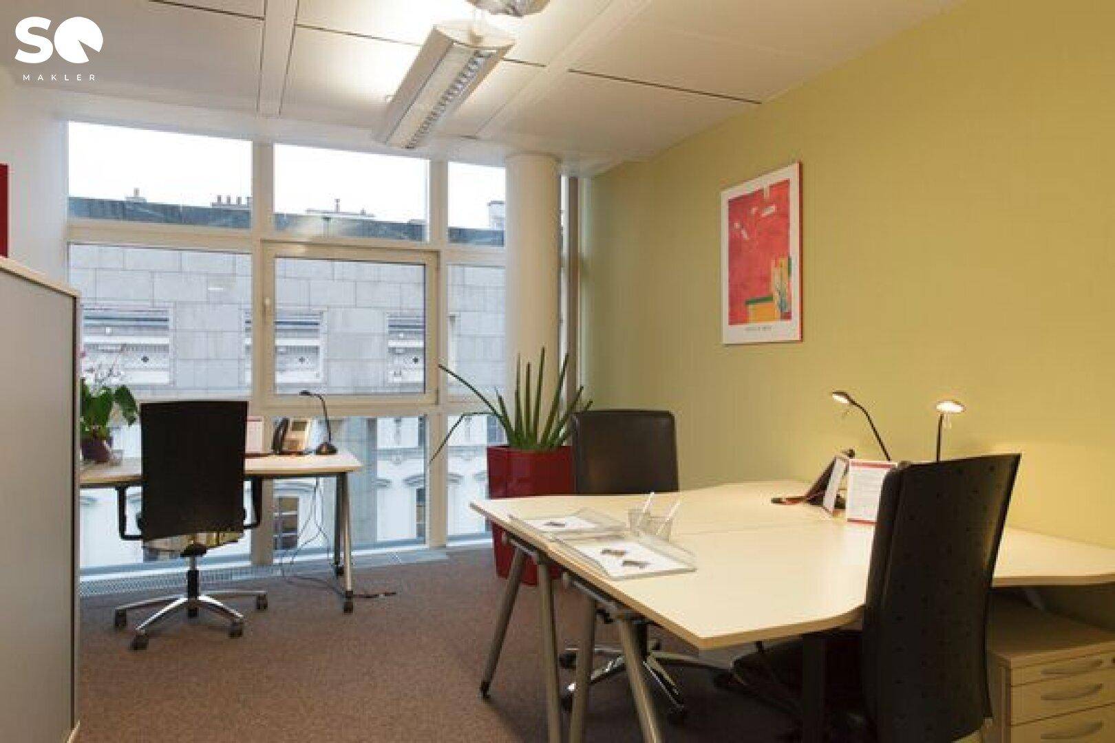 Modernes Büro mit mehreren Arbeitsplätzen, großen Fenstern und einer hellgrünen Wand für eine angenehme Atmosphäre.