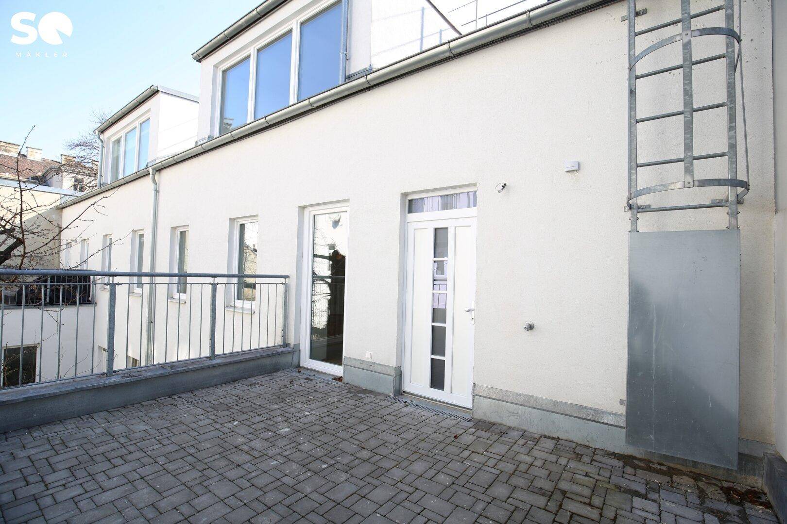 Gepflasterte Terrasse mit Zugang zum Gebäude und einer externen Metallleiter.