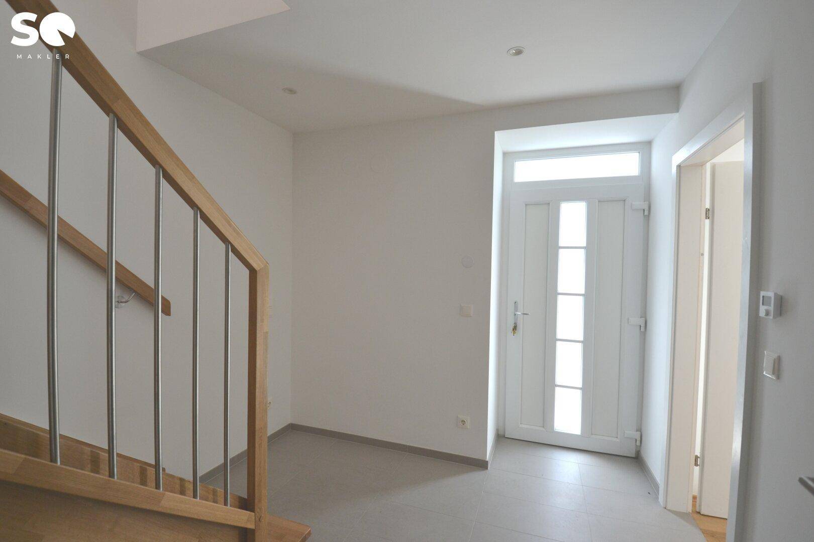 Heller Eingangsbereich mit moderner Holztreppe und weißer Eingangstür.