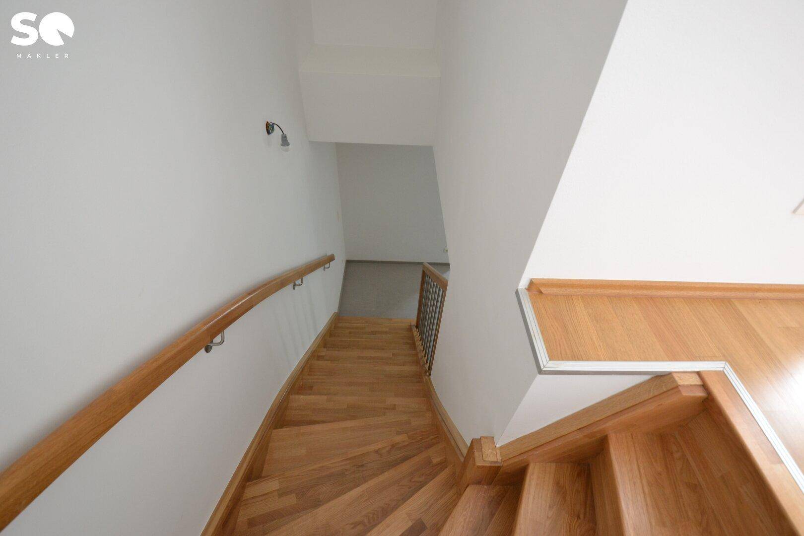 Helle Holztreppe mit Handlauf, die in die untere Etage führt.