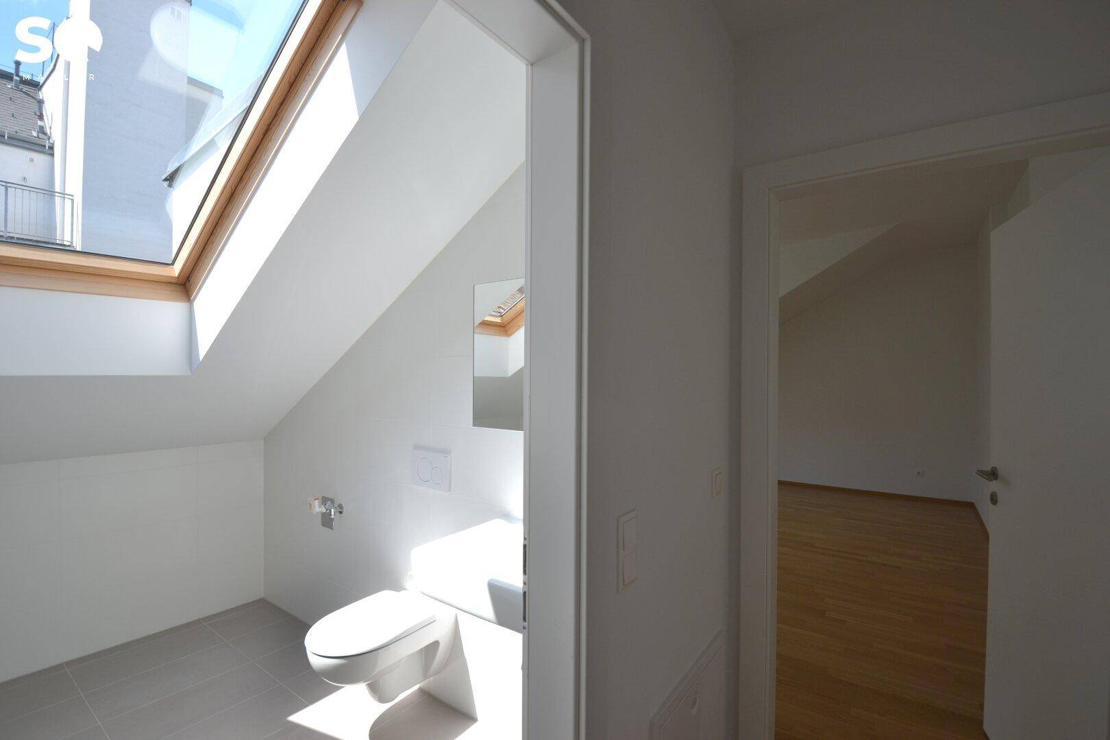 Helles WC im Dachgeschoss mit großem Dachfenster und moderner Toilette.