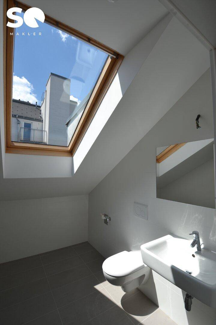 Modernes WC im Dachgeschoss mit großem Dachfenster, Waschbecken und Toilette.