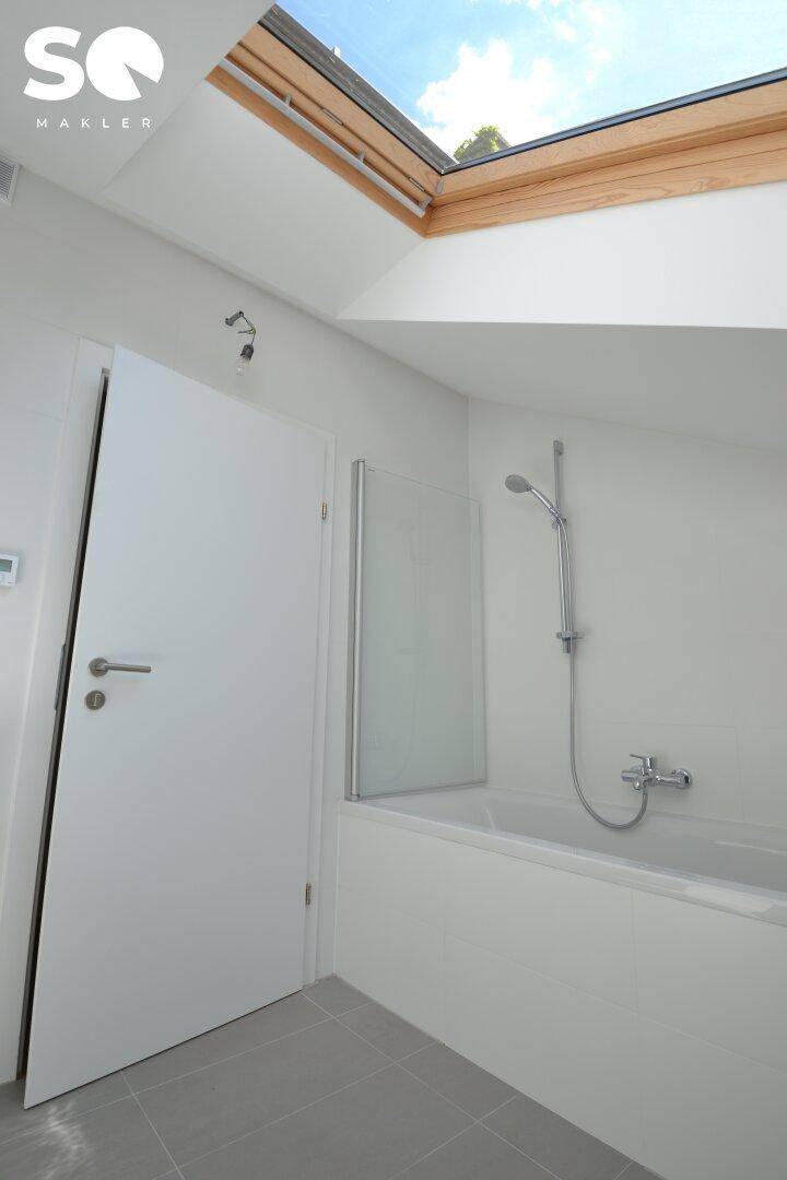 Helles Badezimmer im Dachgeschoss mit Badewanne und großem Dachfenster.