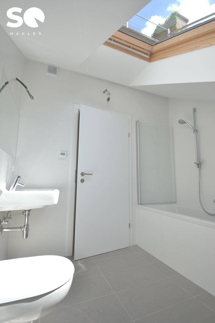 Modernes Badezimmer im Dachgeschoss mit Badewanne, WC, Waschbecken und Dachfenster.