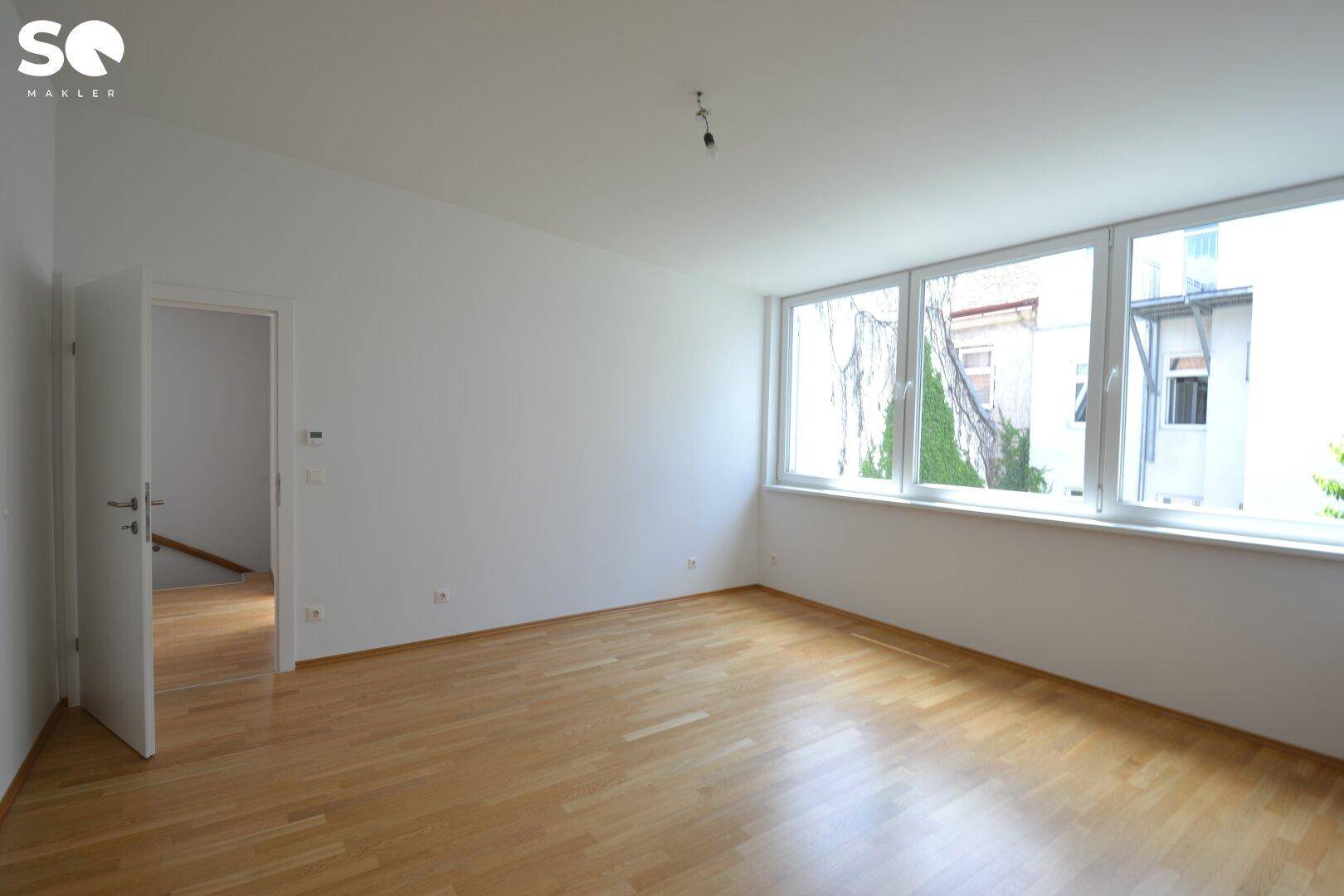 Helles Zimmer mit Parkettboden und großen Fenstern, bereit zur individuellen Gestaltung.