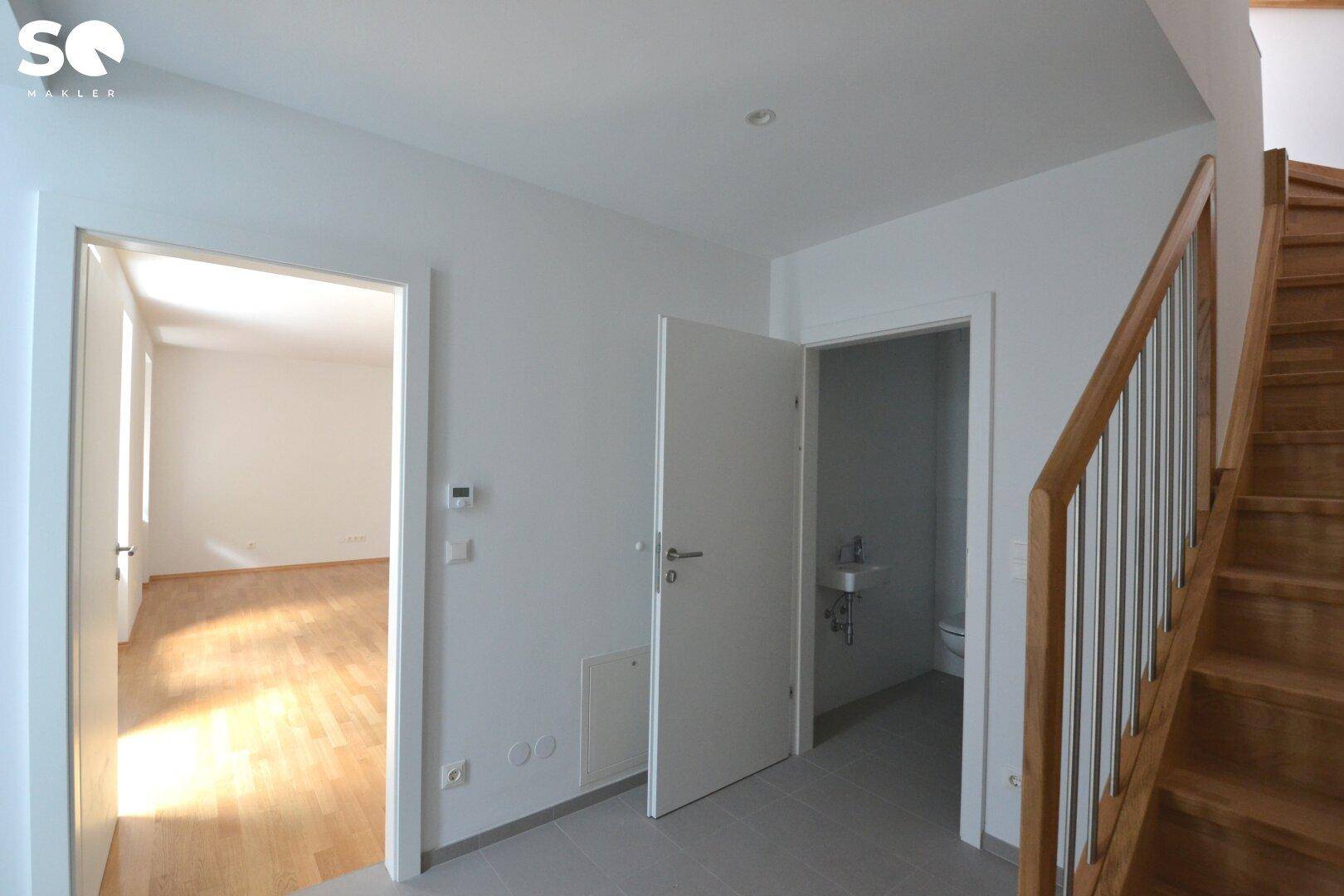 Flur mit Holztreppe und Zugang zu einem weiteren Zimmer sowie einem Gäste-WC.