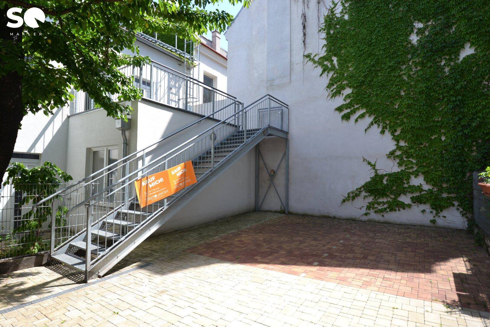 Gepflasterter Innenhof mit Außentreppe und begrünten Wänden.