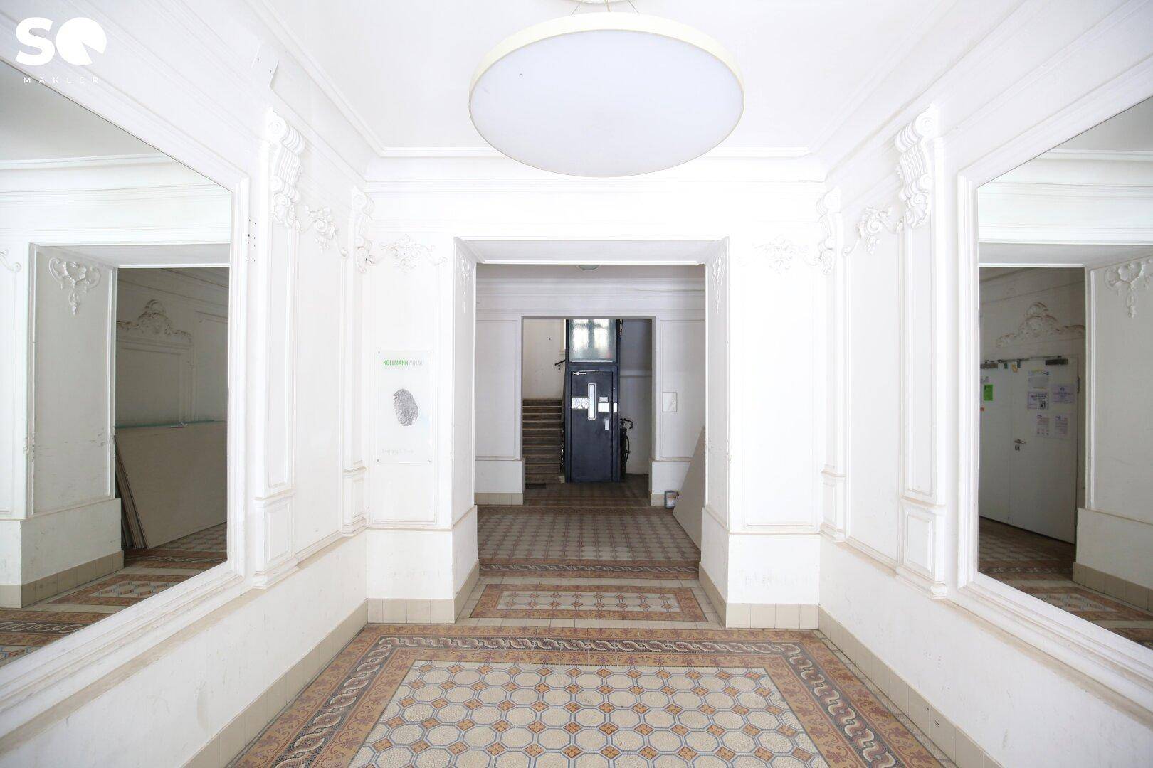 Elegante Eingangshalle mit gemusterten Fliesen, Stuckverzierungen und großen Spiegeln, die zum Treppenhaus führt.