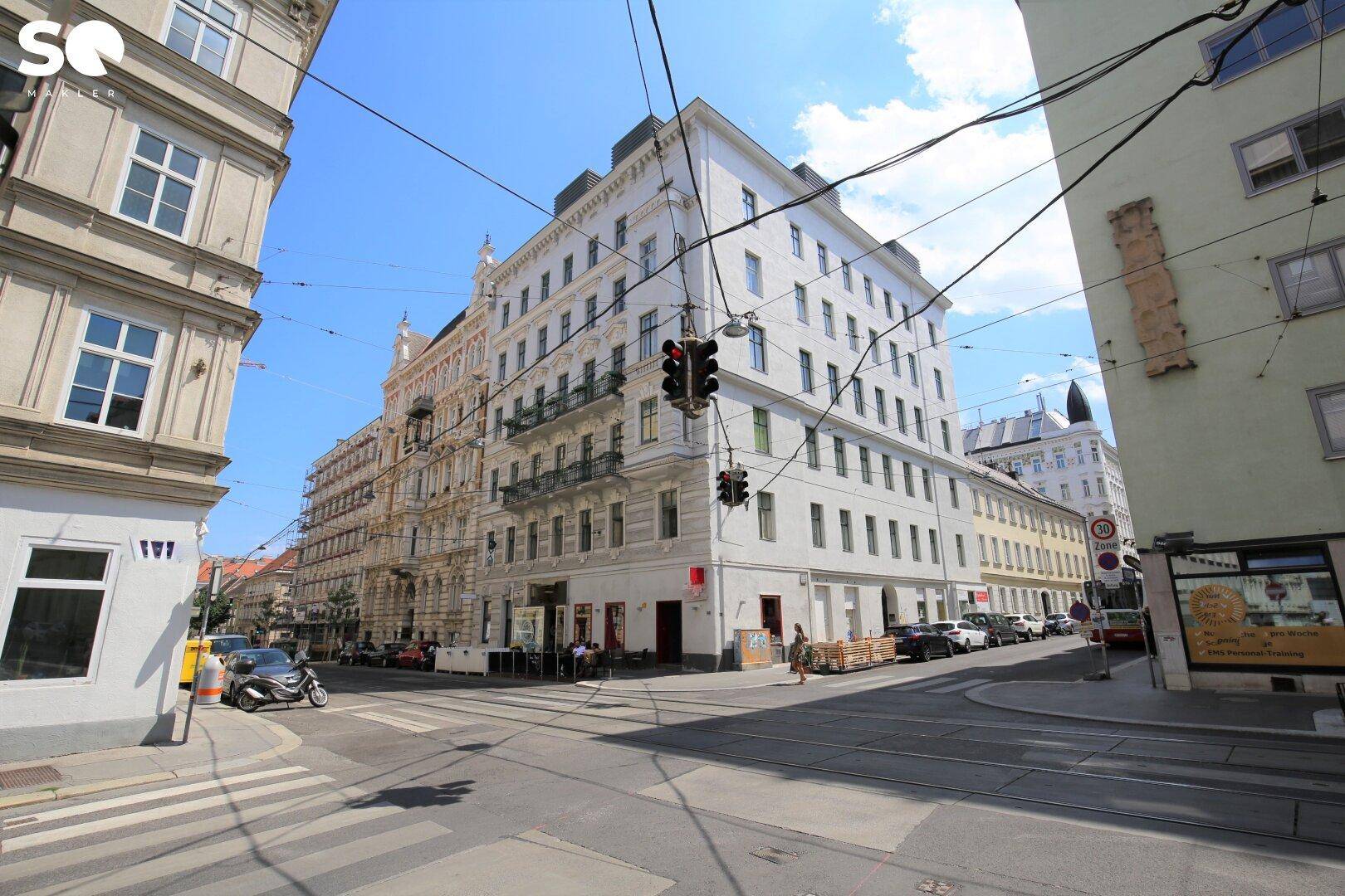 Städtische Straßenszene mit einem Eckgebäude und umliegenden Häusern unter blauem Himmel.