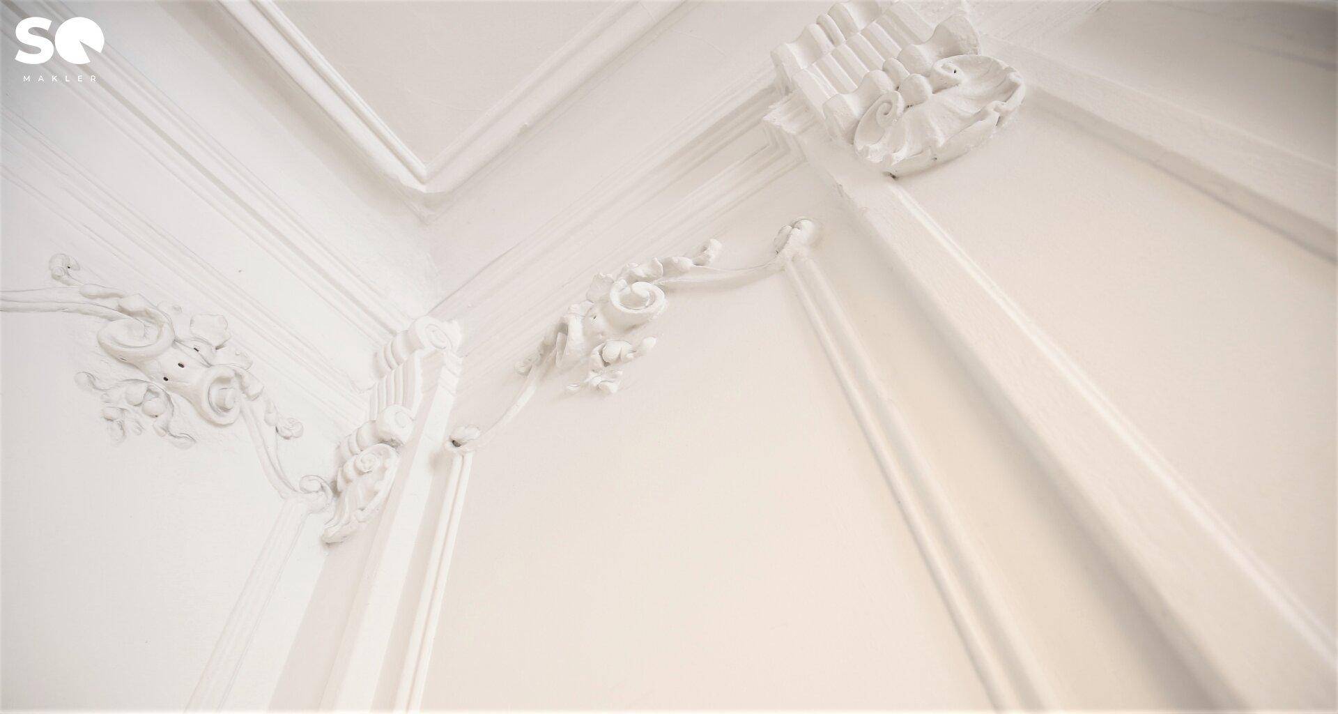 Nahaufnahme von aufwendigen weißen Stuckverzierungen an Wand und Decke, die klassische Eleganz zeigen.
