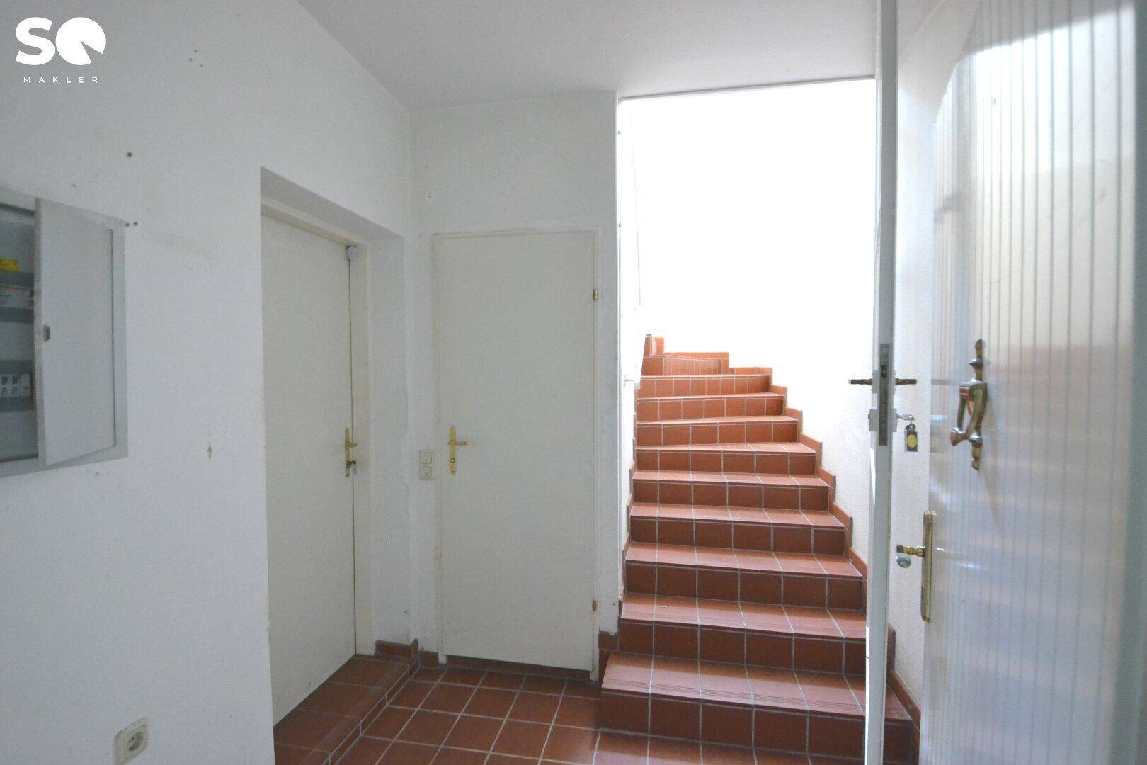 Eingangsbereich mit Terrakotta-Fliesenboden und Treppe zum Obergeschoss.