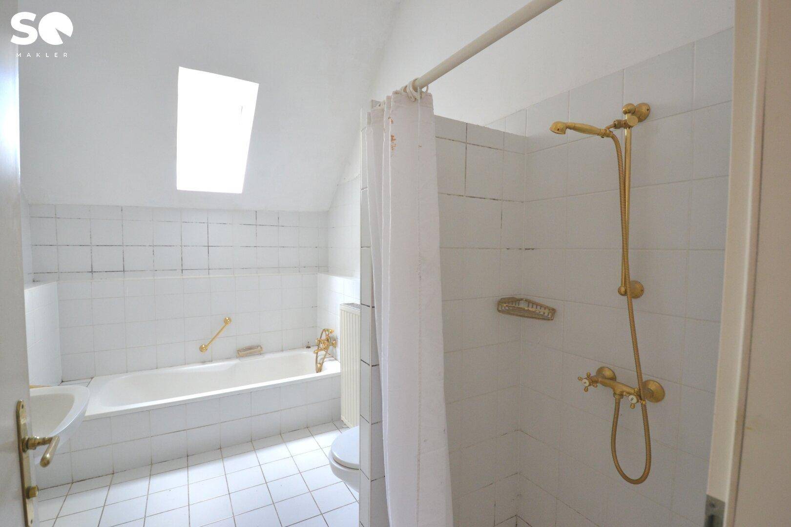 Badezimmer mit Badewanne, Dusche, weißen Fliesen und einem Dachfenster.