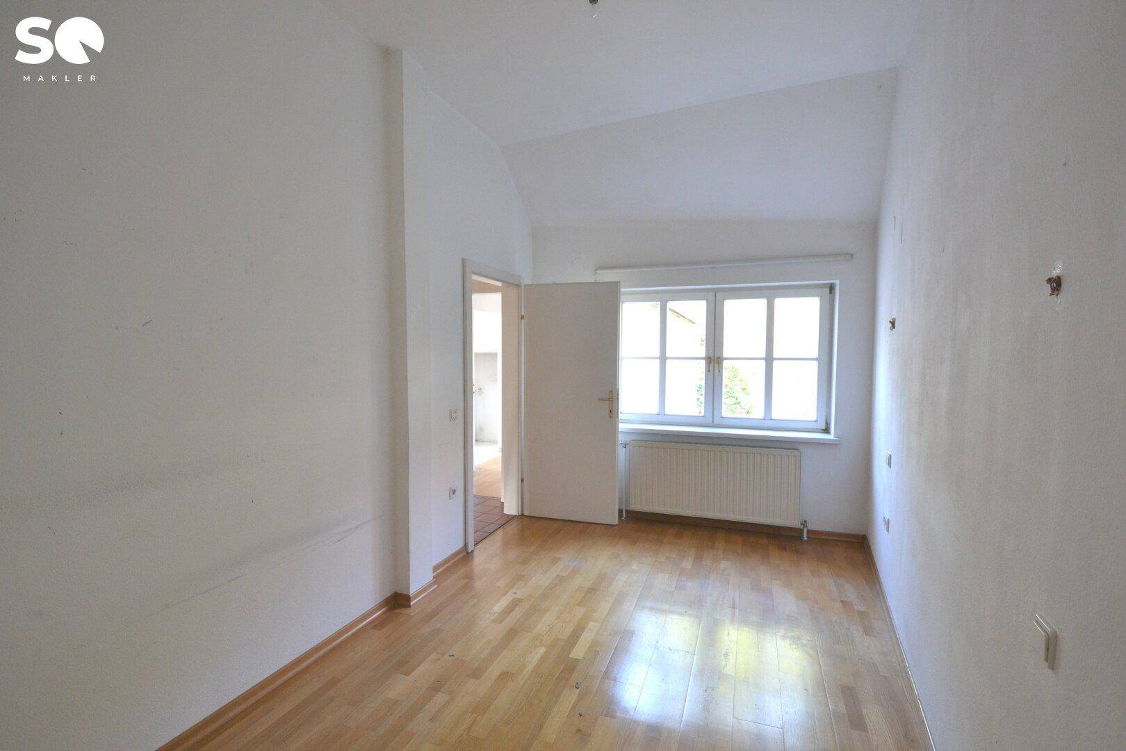 Helles Schlafzimmer mit Holzboden und Fenster, das viel Tageslicht hereinlässt.