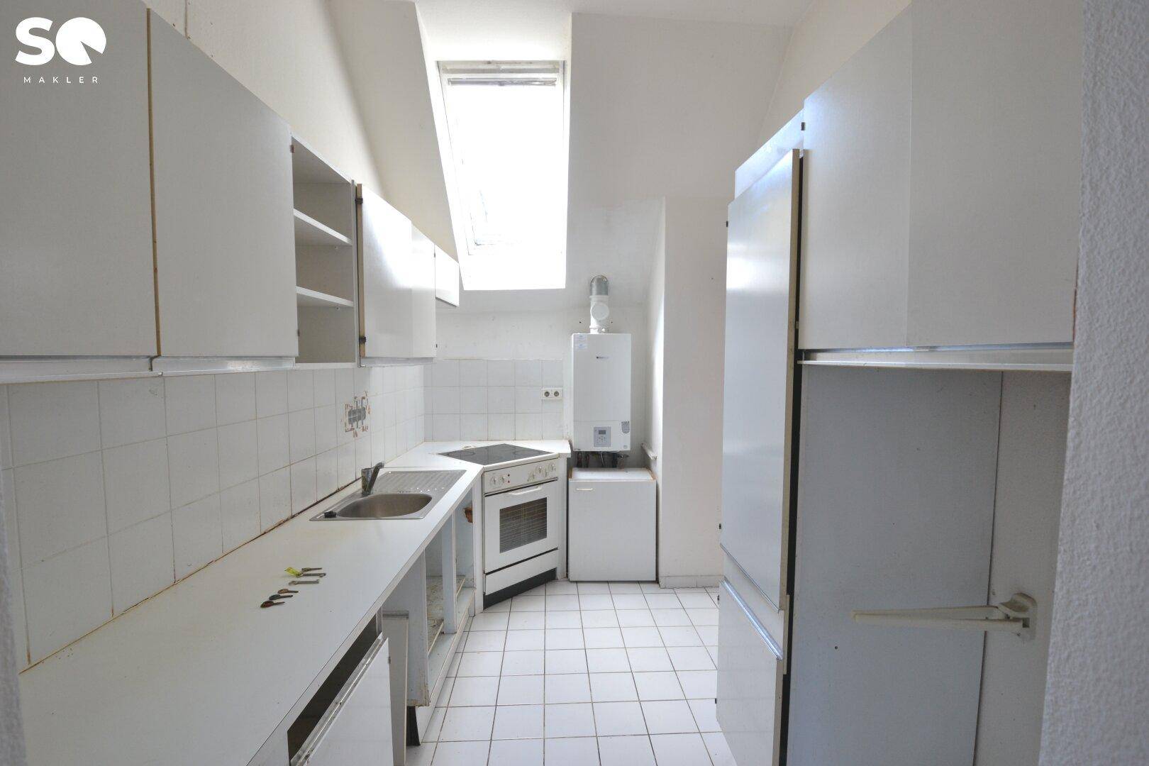 Kleine Küche mit weißen Fliesen, Dachfenster und grundlegenden Küchengeräten.
