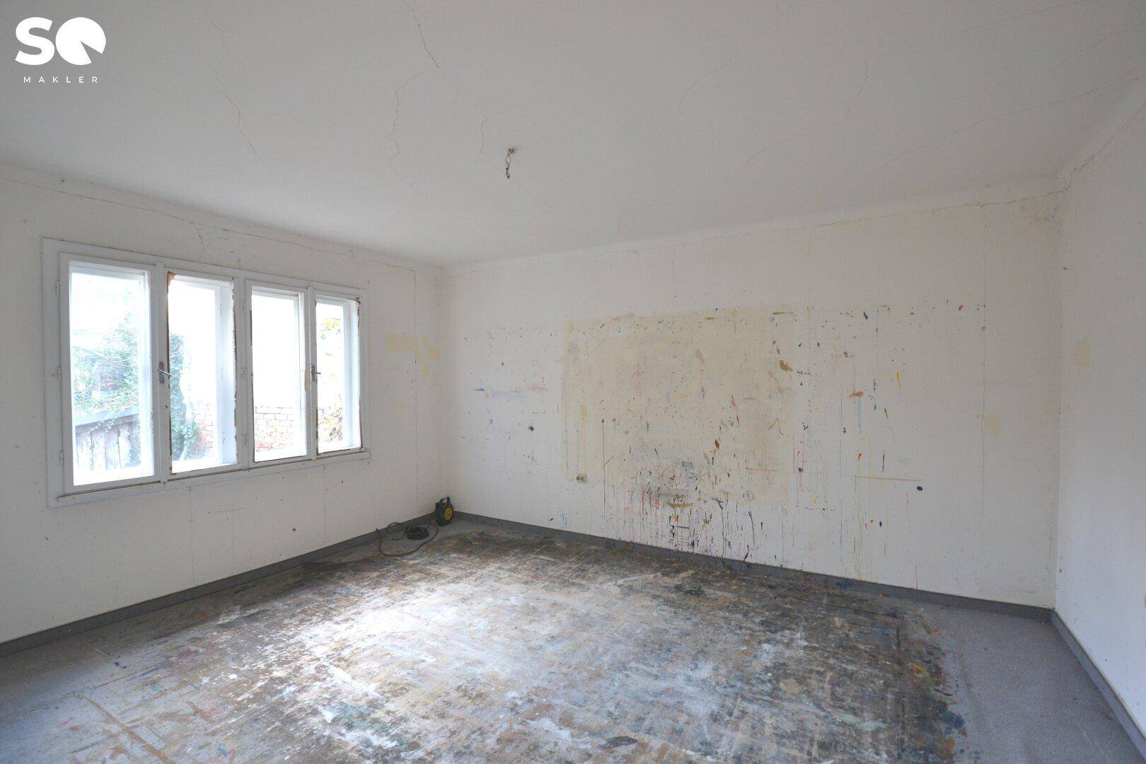 Leerer Raum in Renovierung mit abgenutztem Boden und großen Fenstern, bereit für die Neugestaltung.