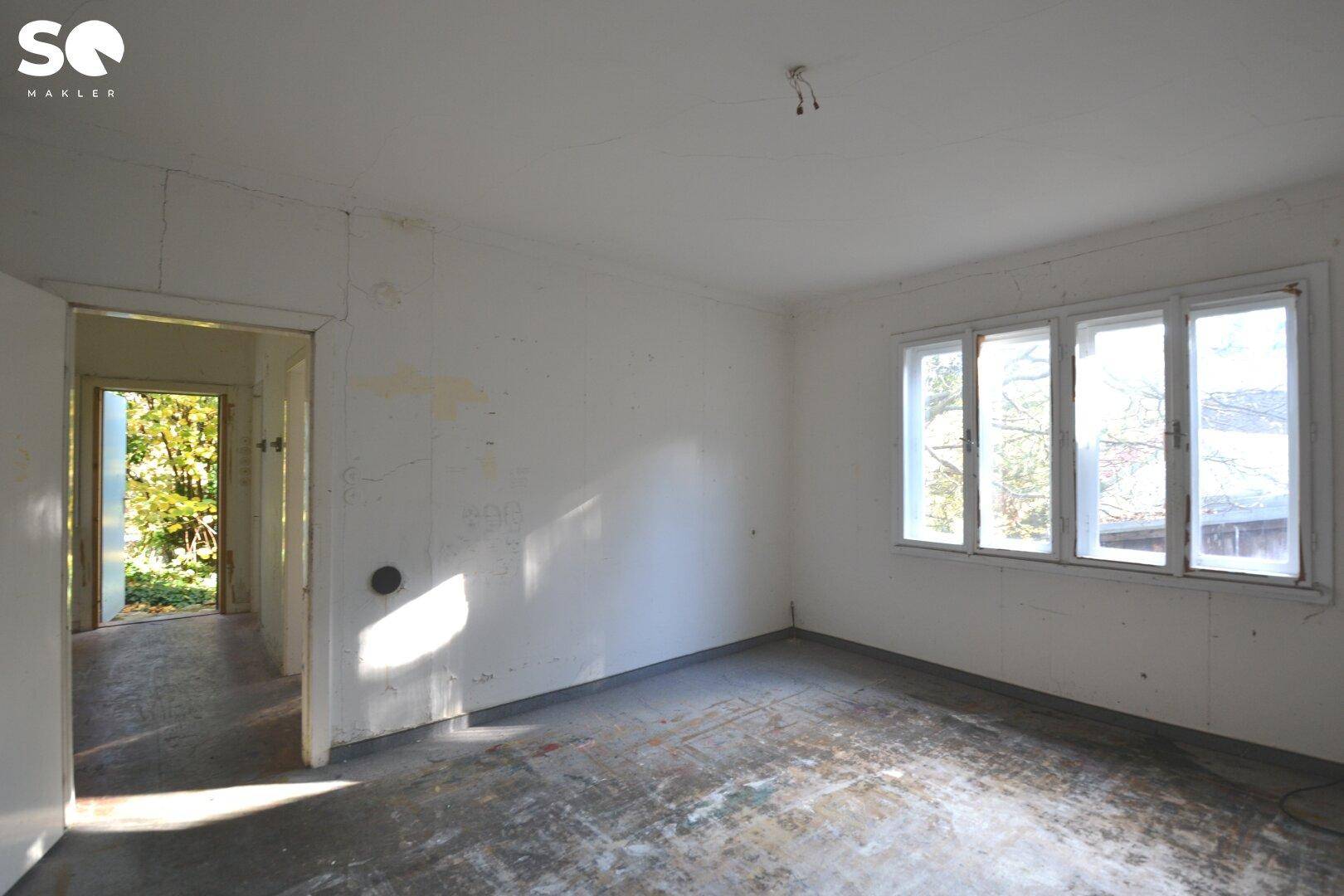 Leerer Raum mit Fenster und abgenutztem Boden, bereit zur Renovierung.