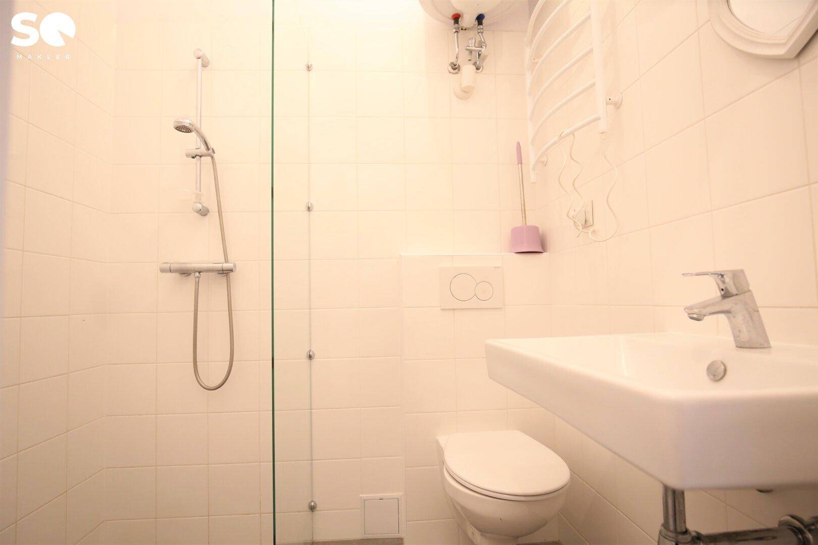 Modernes Badezimmer mit weiß gefliesten Wänden, Dusche, wandhängendem WC und Waschbecken.