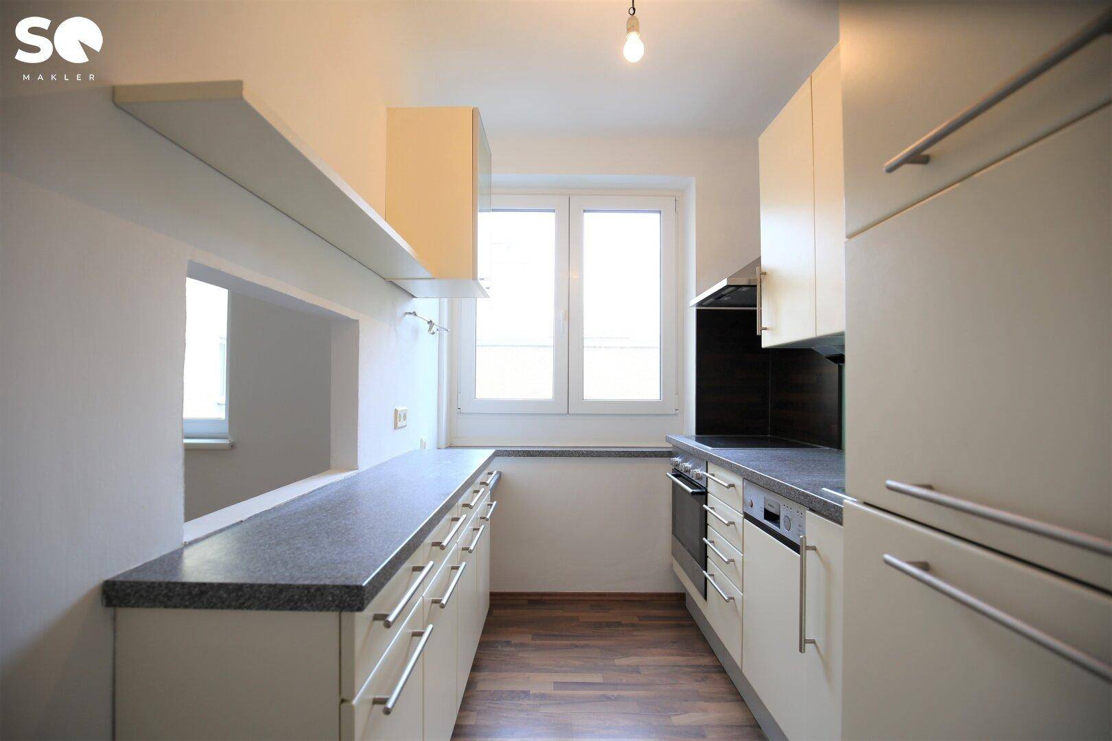 Funktionale Küche mit Einbauschränken, Arbeitsplatte und Fenster zum Essbereich.