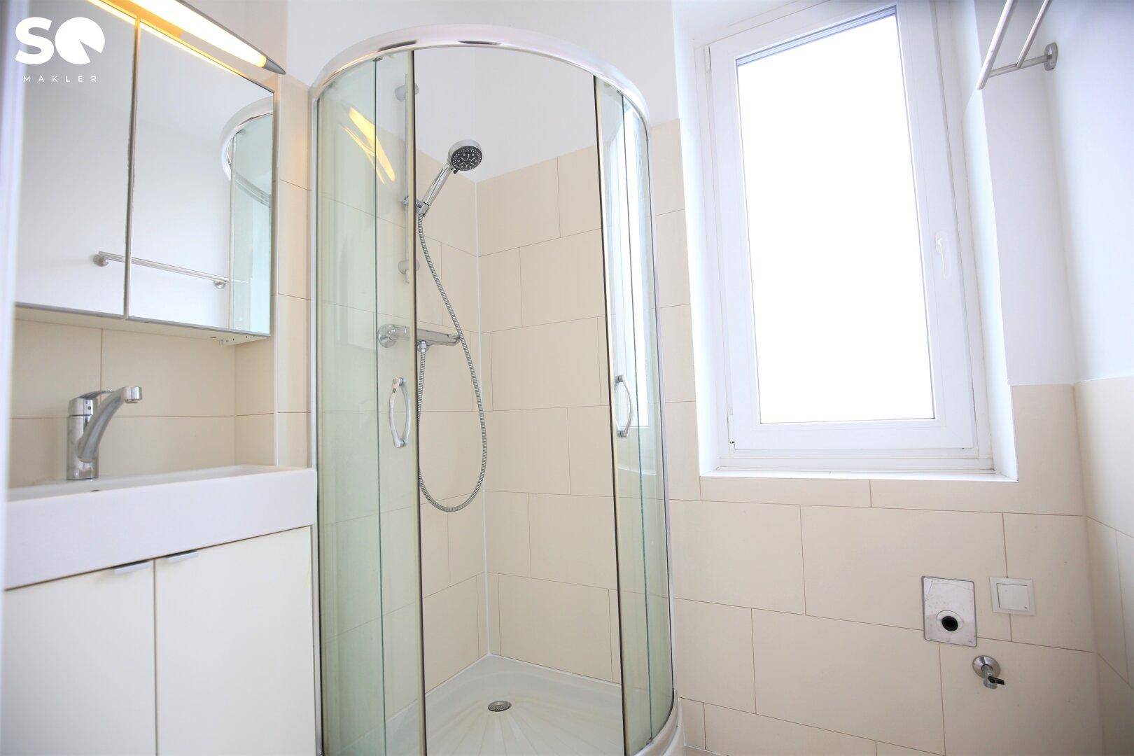 Helles Badezimmer mit Duschkabine, Waschbecken, Spiegelschrank und Fenster.