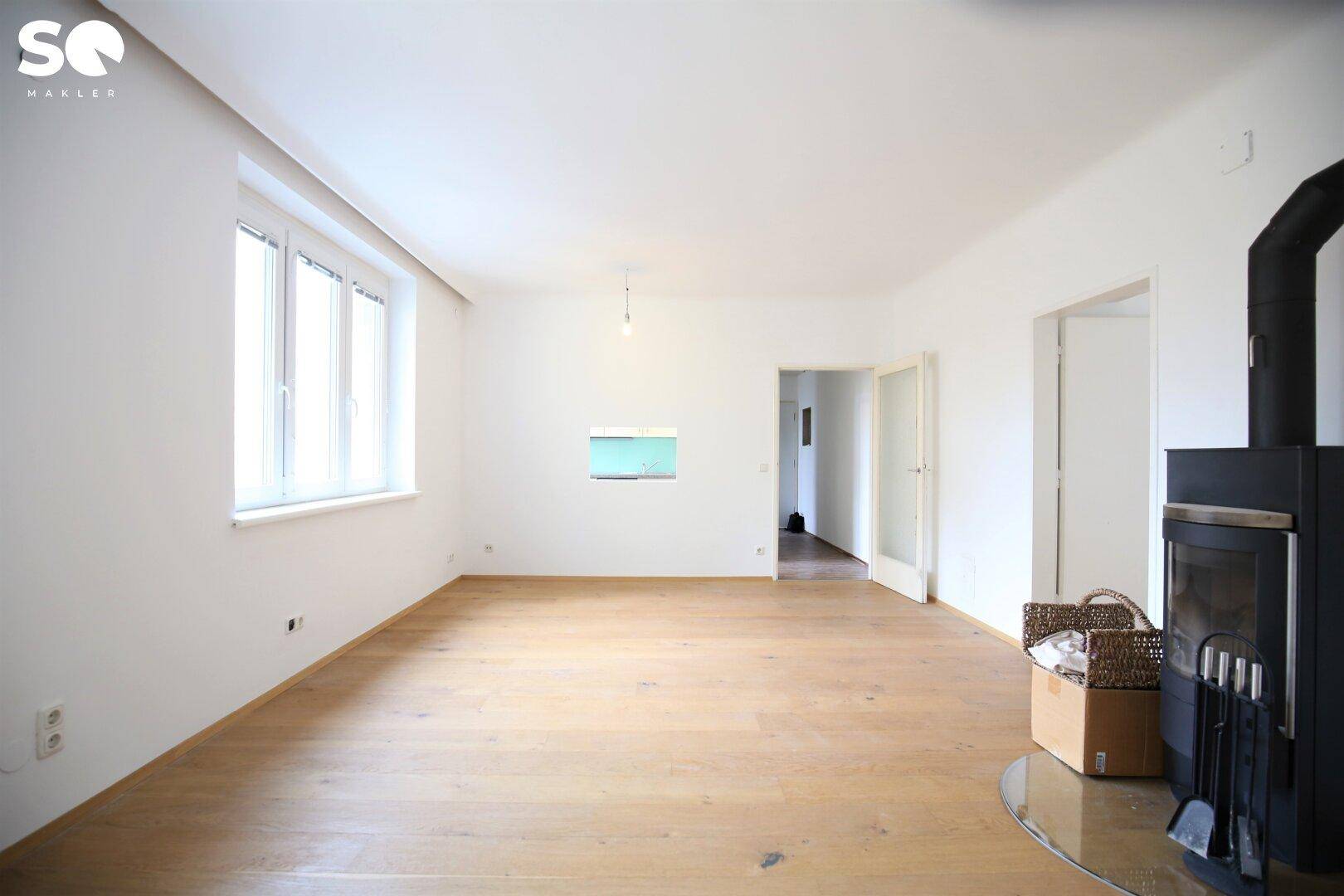 Geräumiges Wohnzimmer mit Holzboden, Kaminofen und Zugang zu weiteren Räumen.