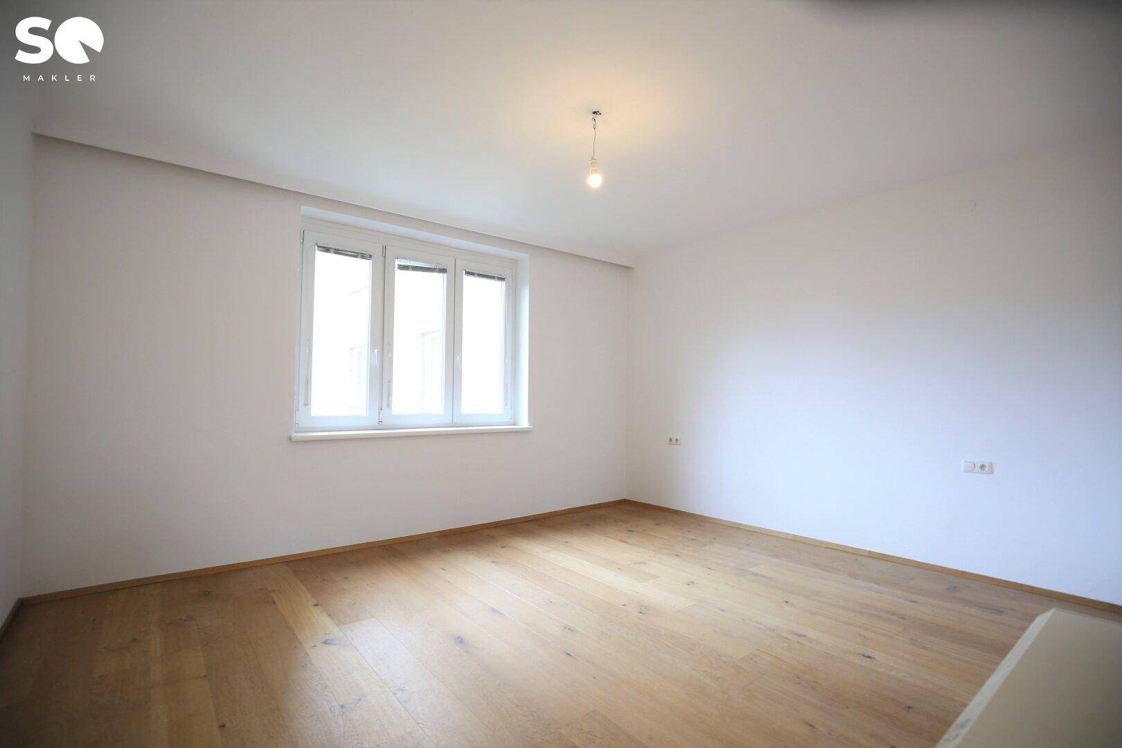 Helles Schlafzimmer mit Holzboden und großem Fenster.