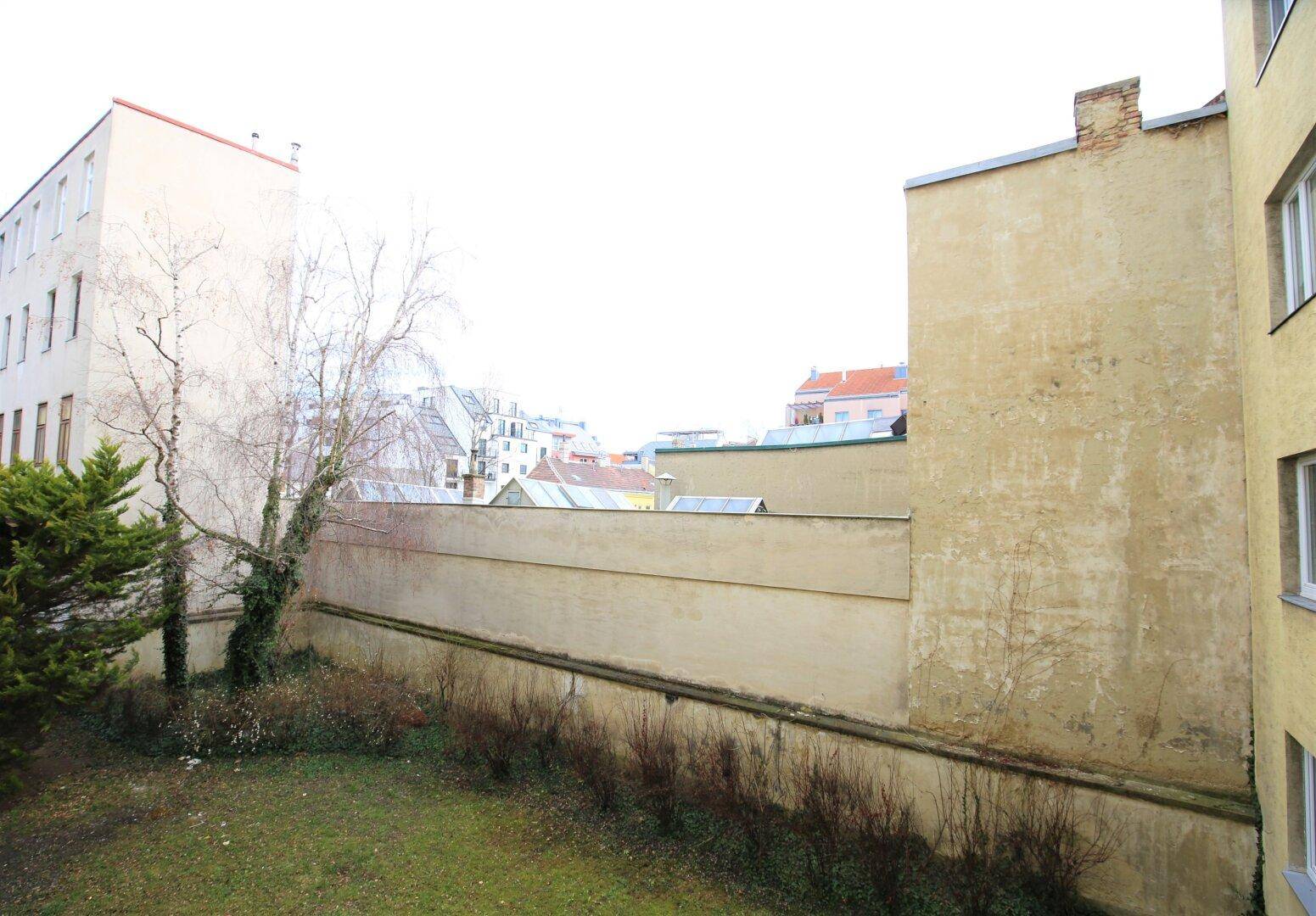 Blick auf einen begrünten Gartenbereich mit Bäumen und umliegenden Gebäuden.