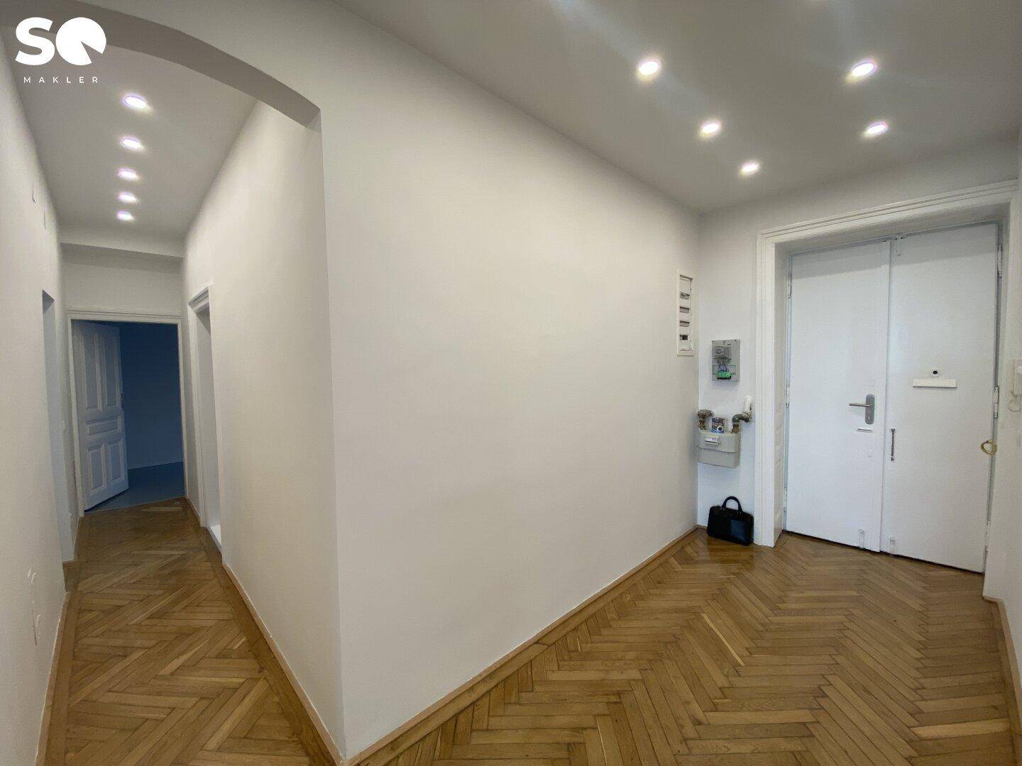 Heller Flur mit Fischgrätparkett, weißen Wänden und moderner Einbauleuchten an der Decke.