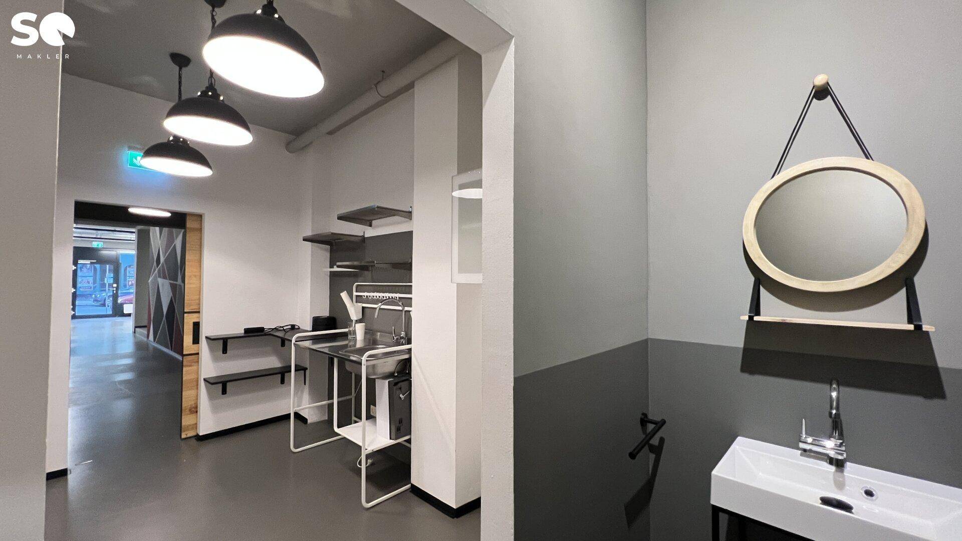 Funktionaler Hauswirtschaftsraum mit Spülbecken, Regalen, Pendelleuchten und einem runden Wandspiegel.