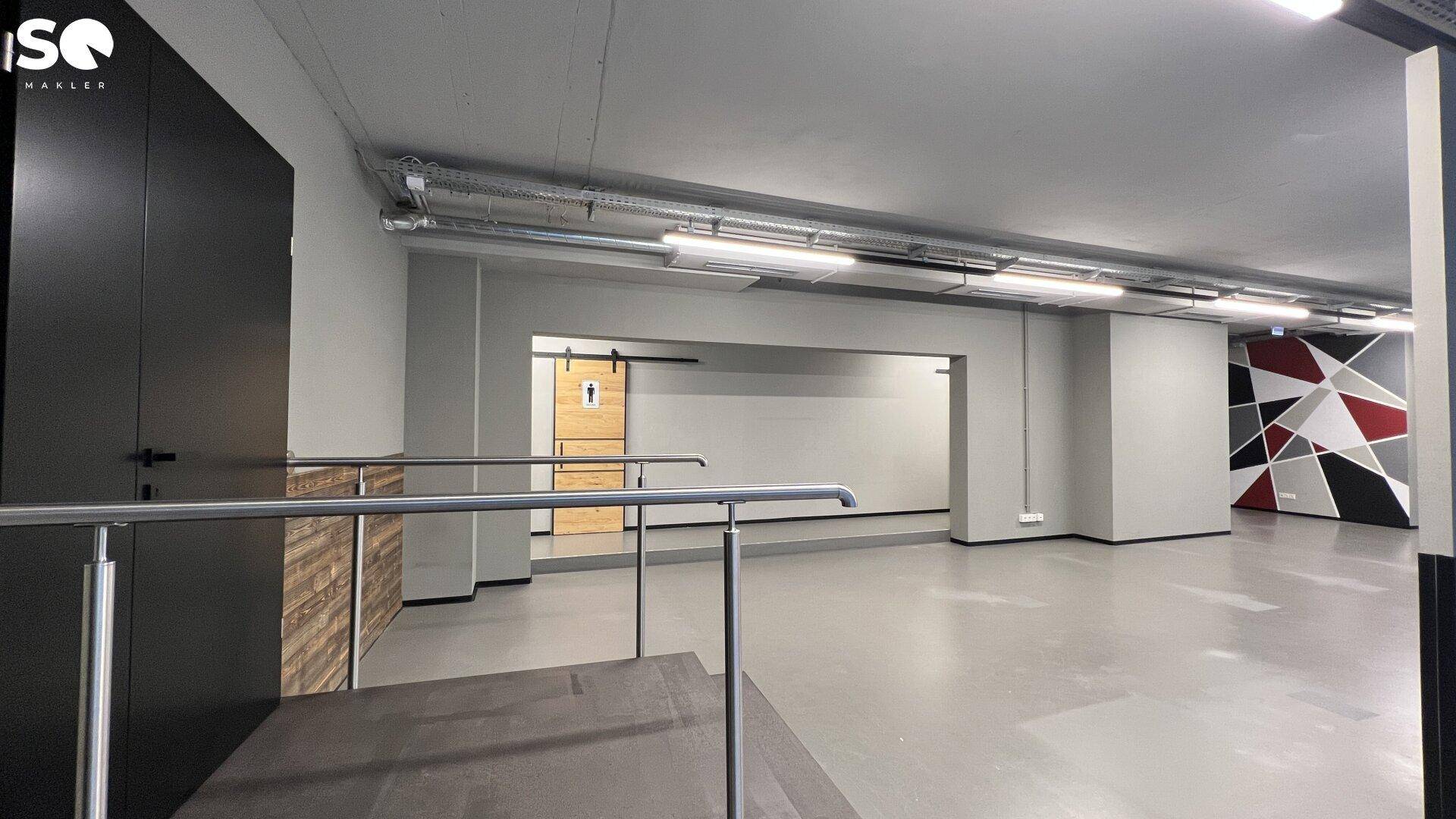 Innenansicht eines Gewerberaums mit Treppe, Metallgeländer und einer rustikalen Holzschiebetür im Hintergrund.