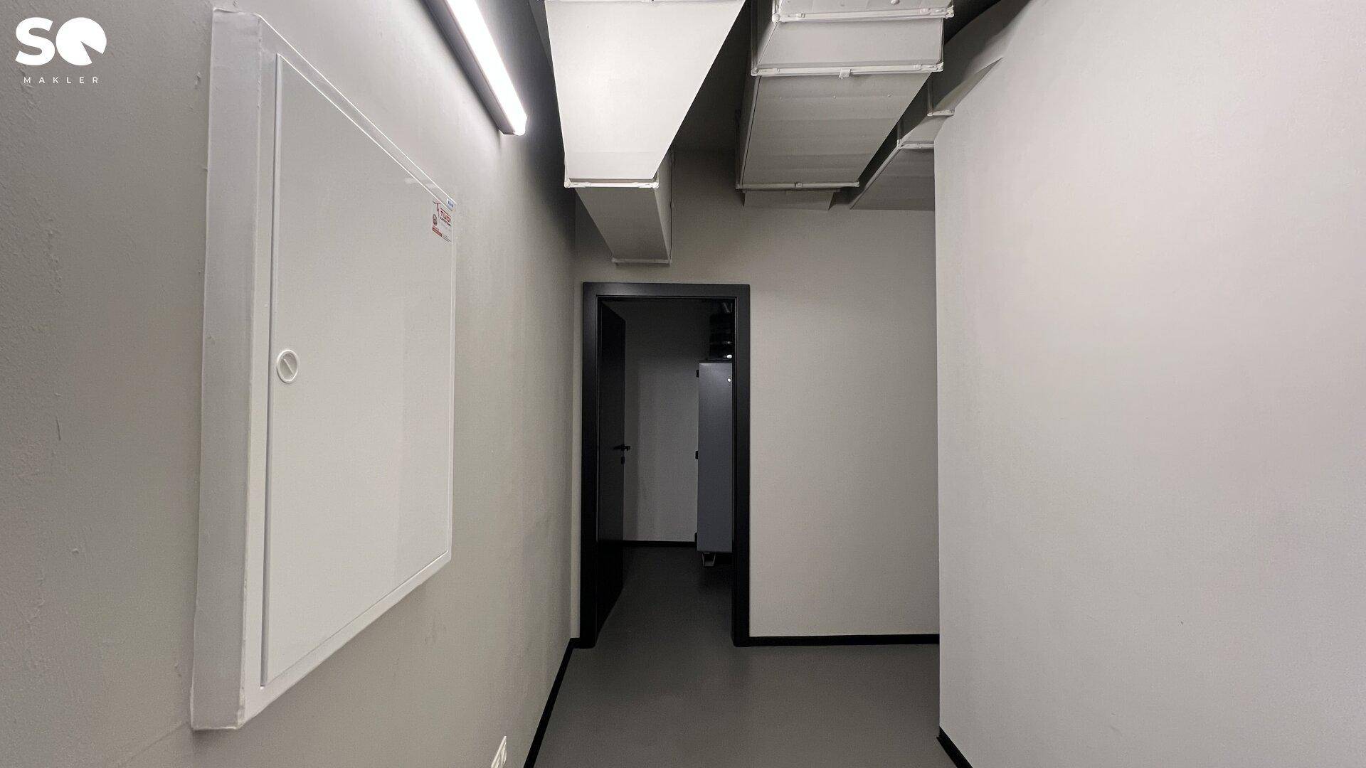 Schlichter Flur oder Technikbereich mit einer Wandverkleidung und sichtbaren Lüftungskanälen an der Decke.