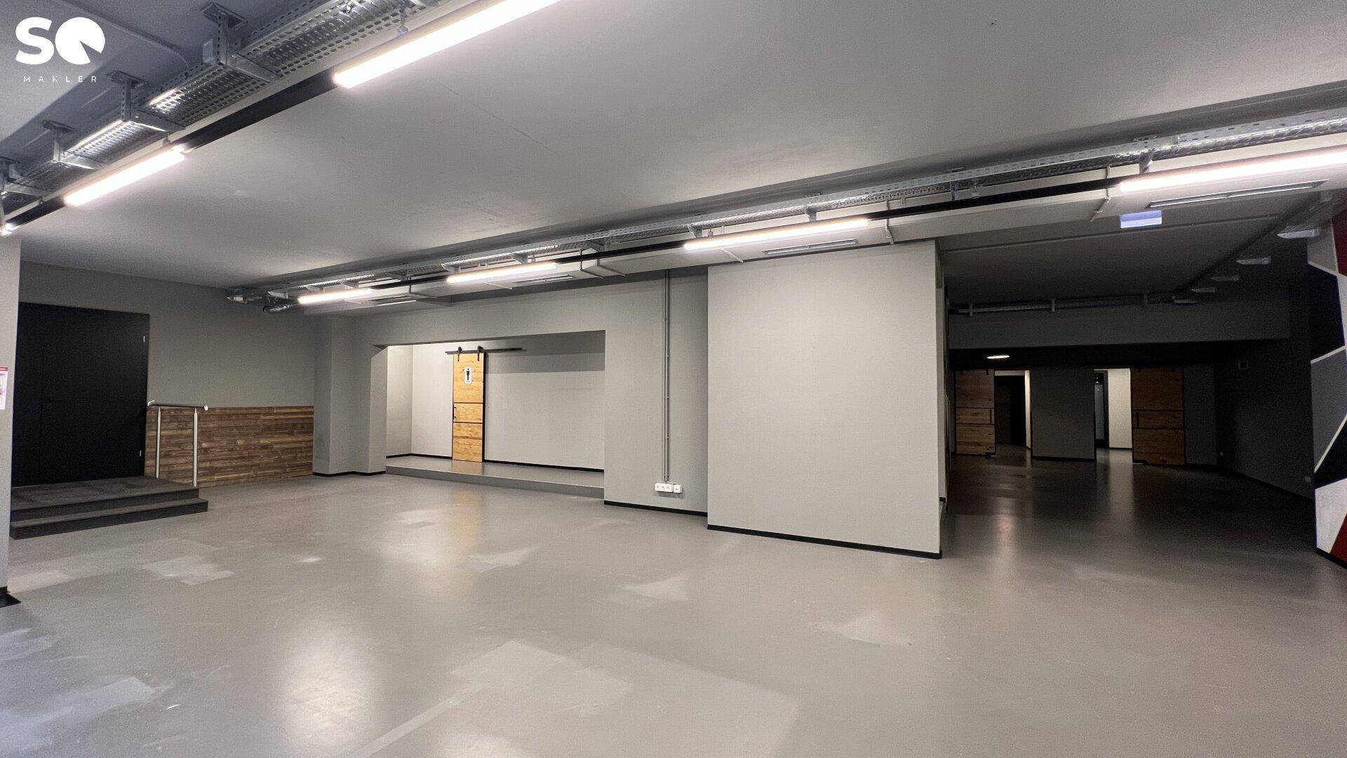 Geräumiger Gewerberaum mit erhöhter Plattform, einer Holzschiebetür und Zugang zu weiteren Bereichen.