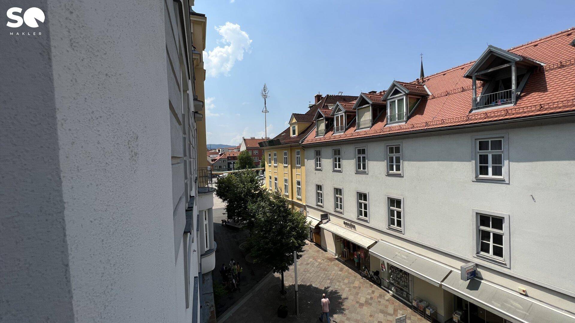 Blick von oben auf eine belebte Einkaufsstraße mit historischen Gebäuden und roten Ziegeldächern.