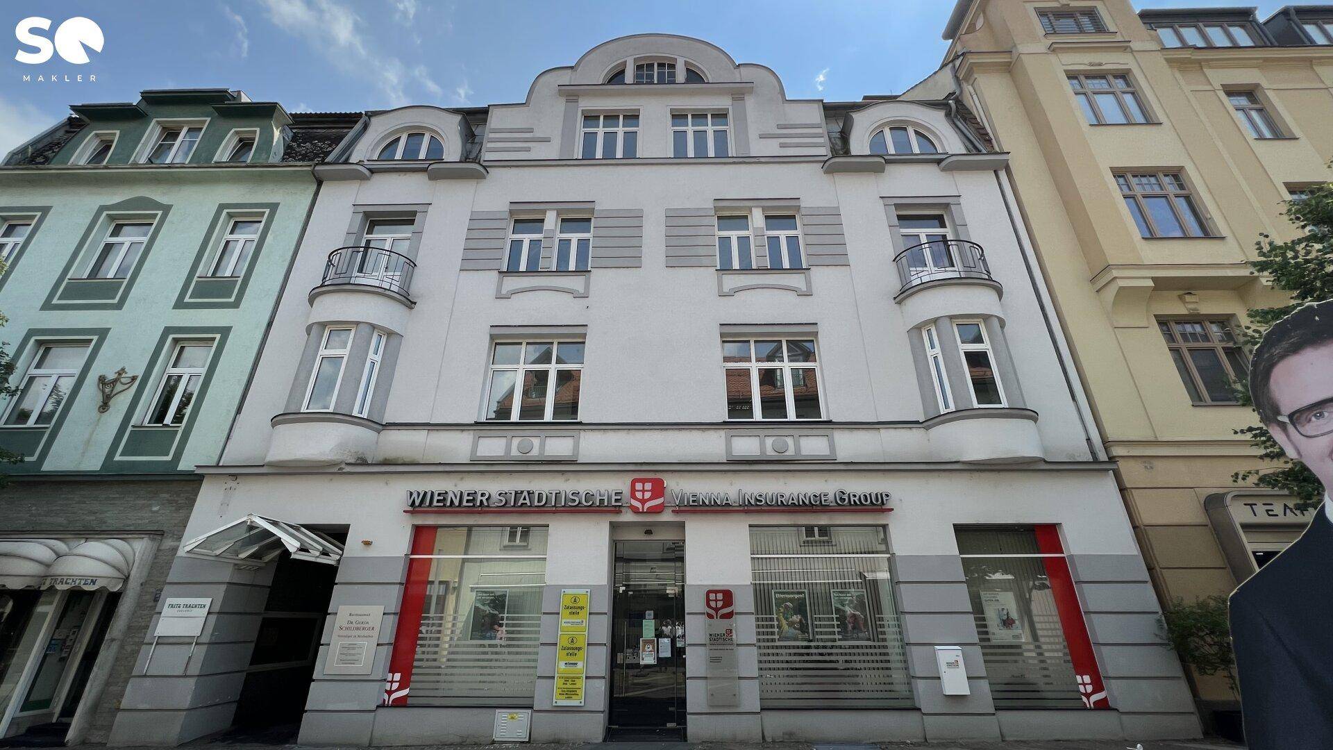 Historisches Gebäude mit klassischer Fassade und Geschäften im Erdgeschoss an einer belebten Straße.