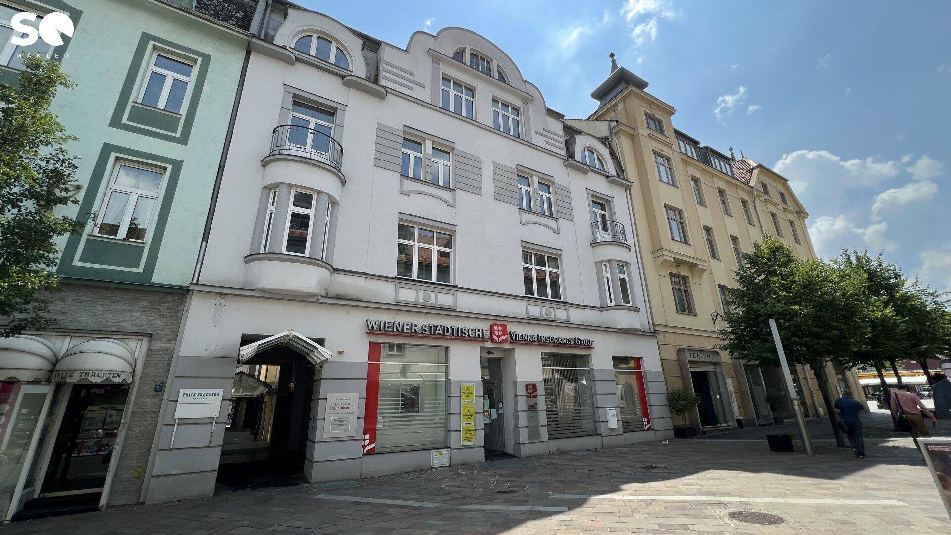 Historisches Gebäude mit klassischer Fassade und Geschäften im Erdgeschoss an einer belebten Straße.
