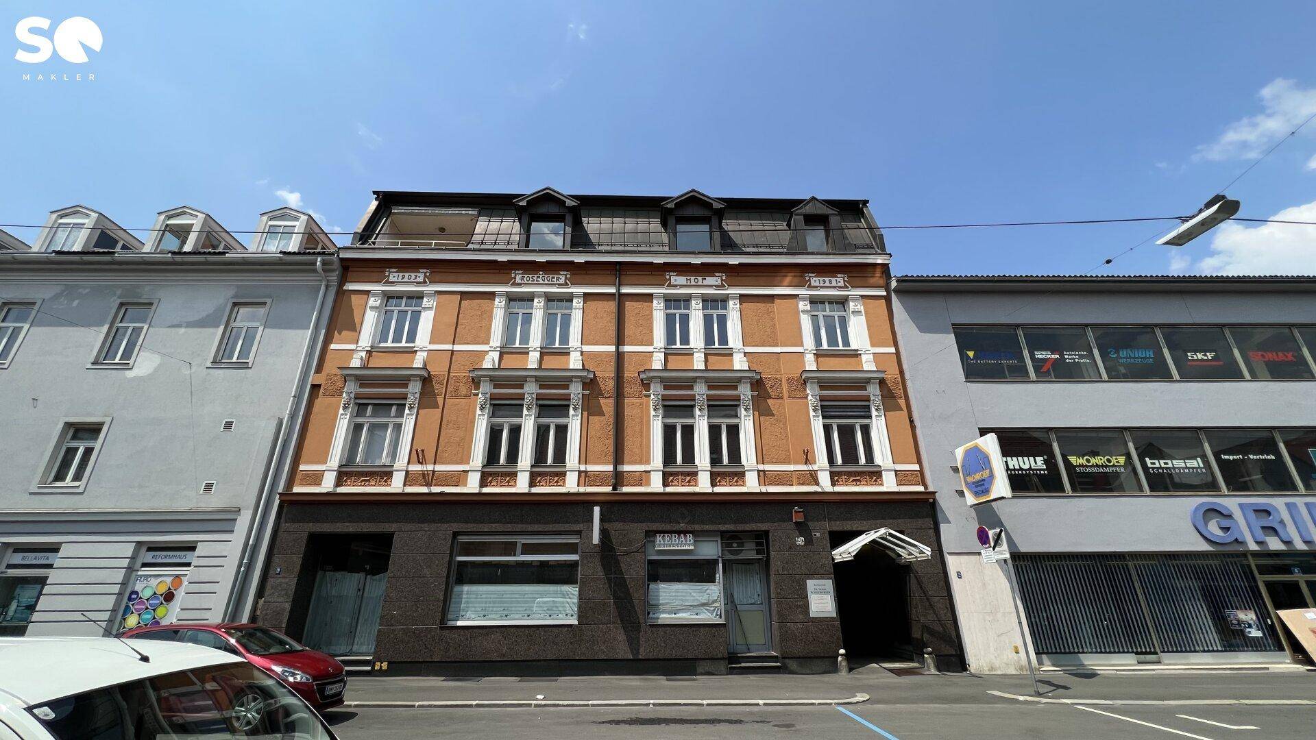 Historisches Gebäude mit orangeroter Fassade und dunklem Erdgeschoss an einer städtischen Straße.