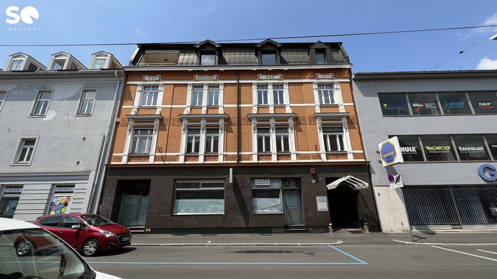 Historisches Gebäude mit orangeroter Fassade und dunklem Erdgeschoss an einer städtischen Straße.