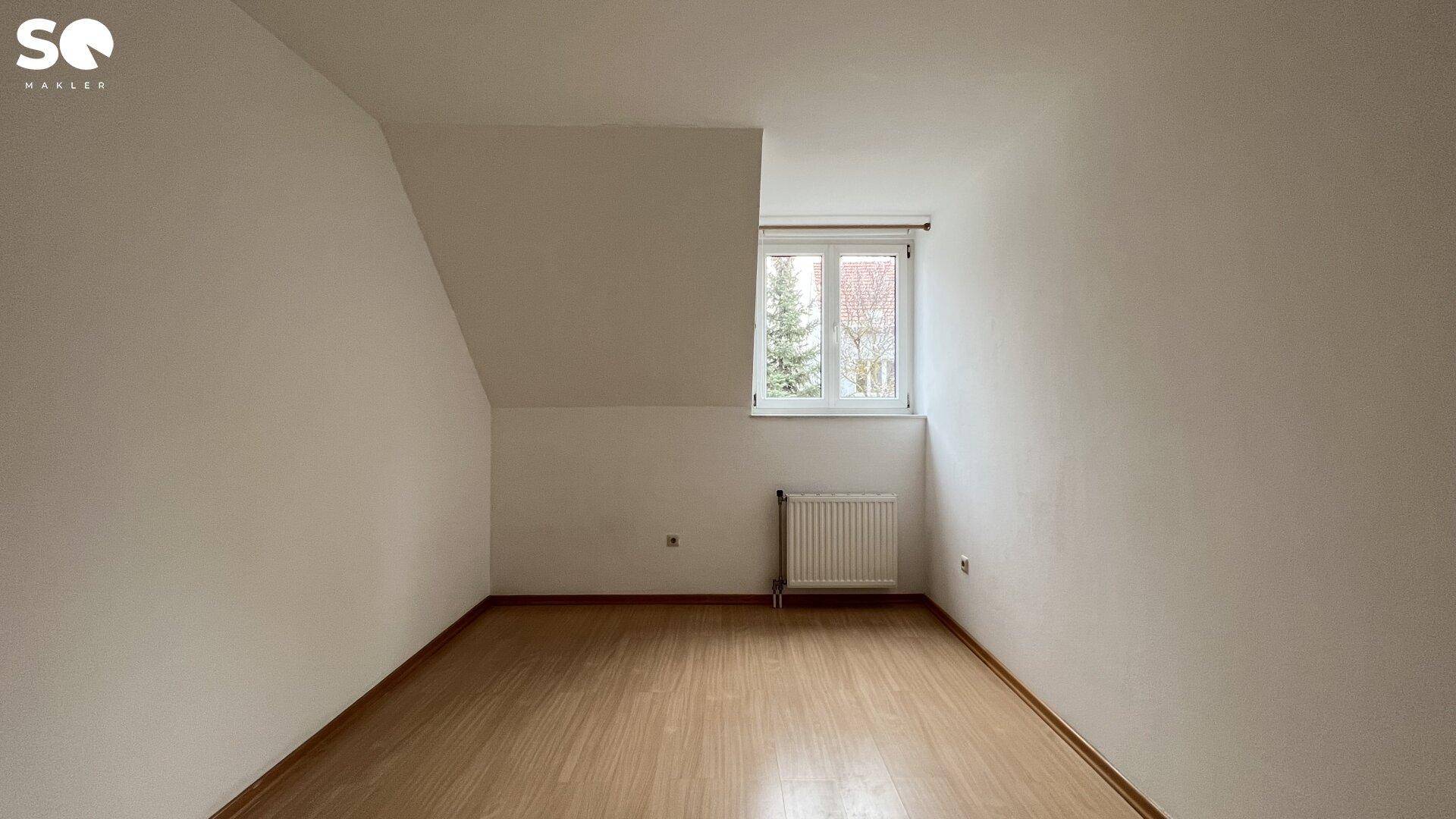 Gemütliches Zimmer mit Holzfußboden, Fenster und einer Dachschräge, ideal als Schlafzimmer.