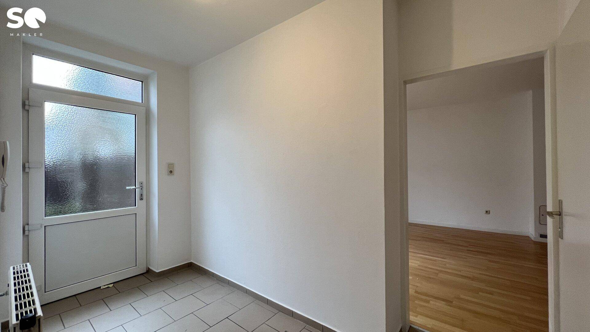 Eingangsbereich mit Fliesenboden und Zugang zu einem weiteren Raum mit Holzfußboden.