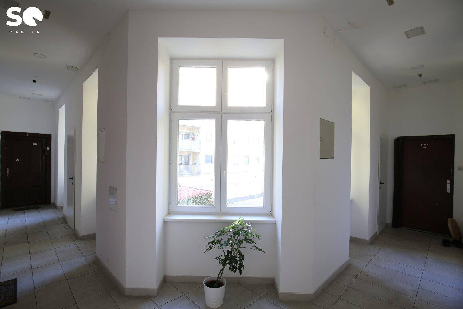 Lichtdurchfluteter Flur mit großem Fenster, Fliesenboden und Topfpflanze als Dekoration.
