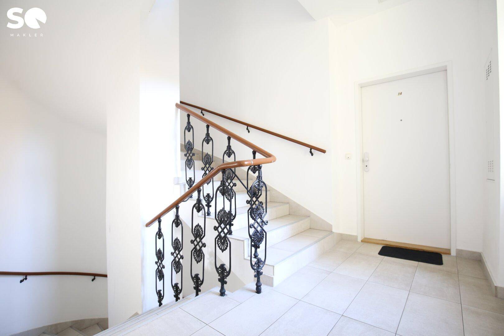 Treppenhaus mit elegantem schmiedeeisernem Geländer und Zugang zu einer Wohnungstür.