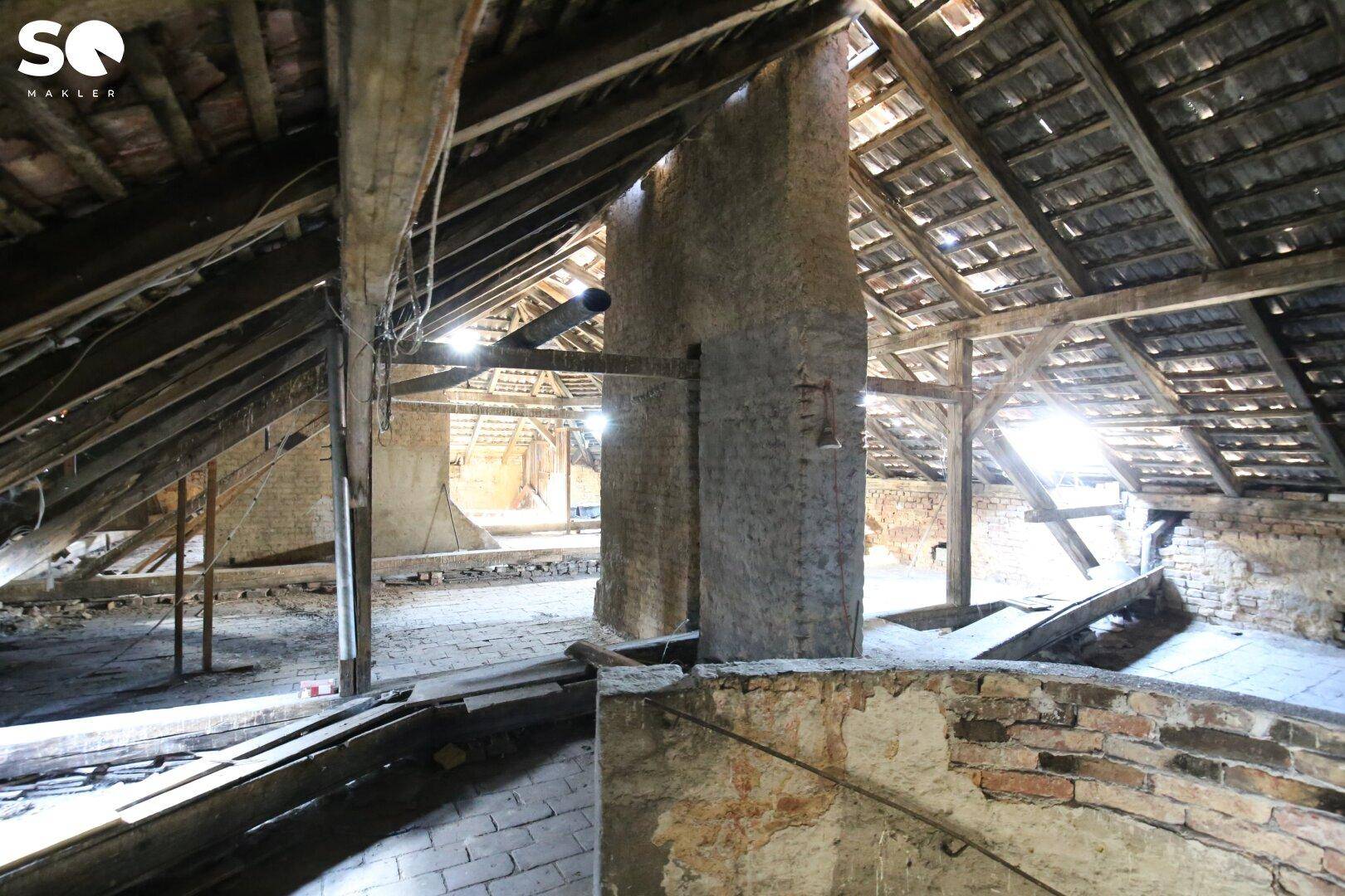 Ungenutzter Dachboden mit sichtbaren Holzbalken, Ziegelwänden und viel natürlichem Licht.