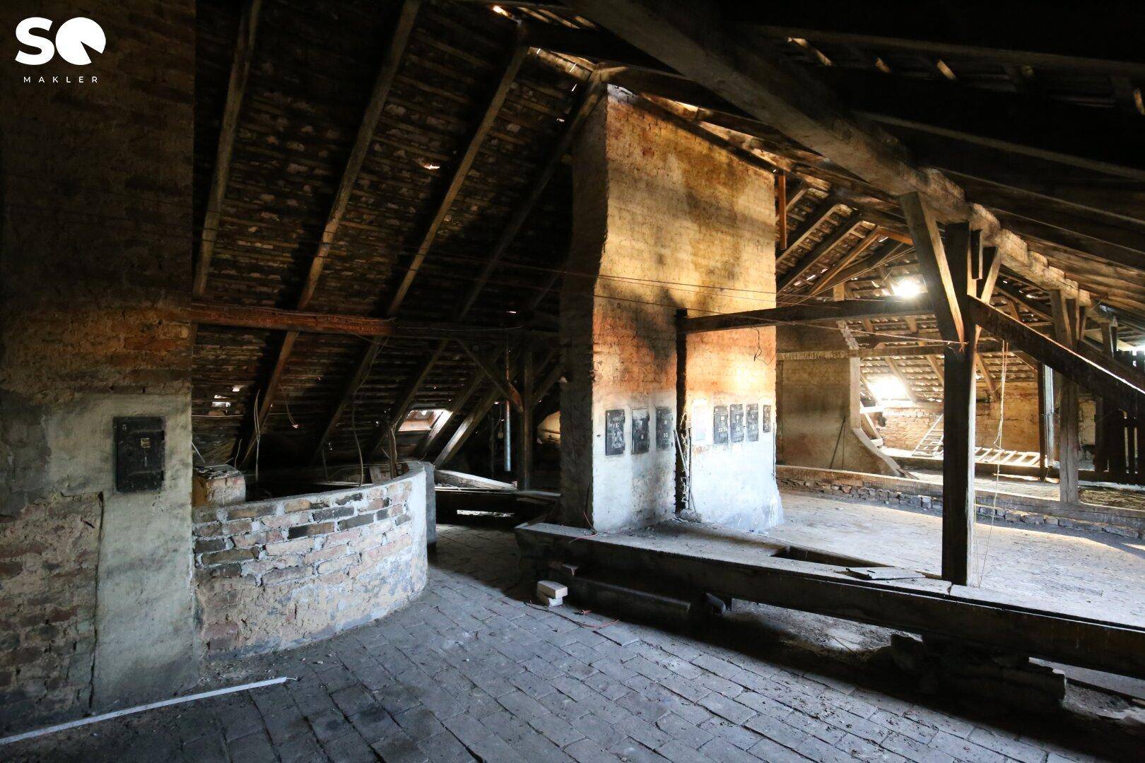 Geräumiger, unausgebauter Dachboden mit freiliegenden Holzbalken und Mauerwerk.