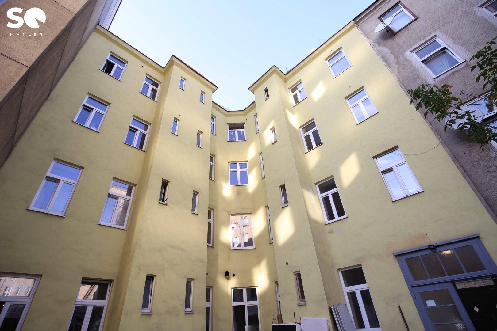 Innenhof des Gebäudes mit gelber Fassade und vielen Fenstern, die nach innen blicken.